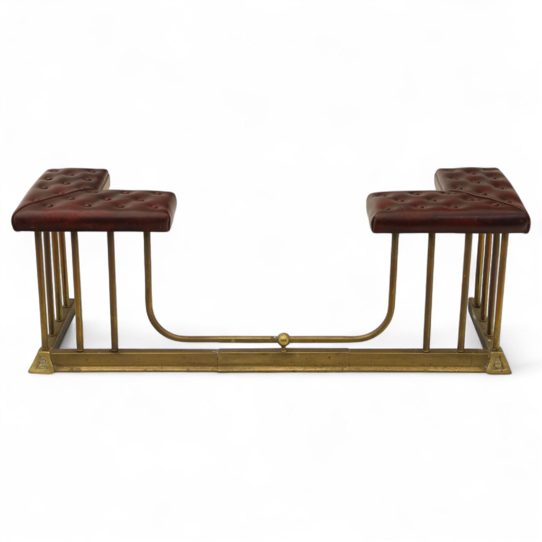 Late Victorian brass and cast iron club fender, burgundy leather buttoned seat pads, secured by bar uprights at the front and back, and a cross stretcher held in place by further bar uprights on a chamfered platform base, circa 1890, internal base dimensions 127cm 