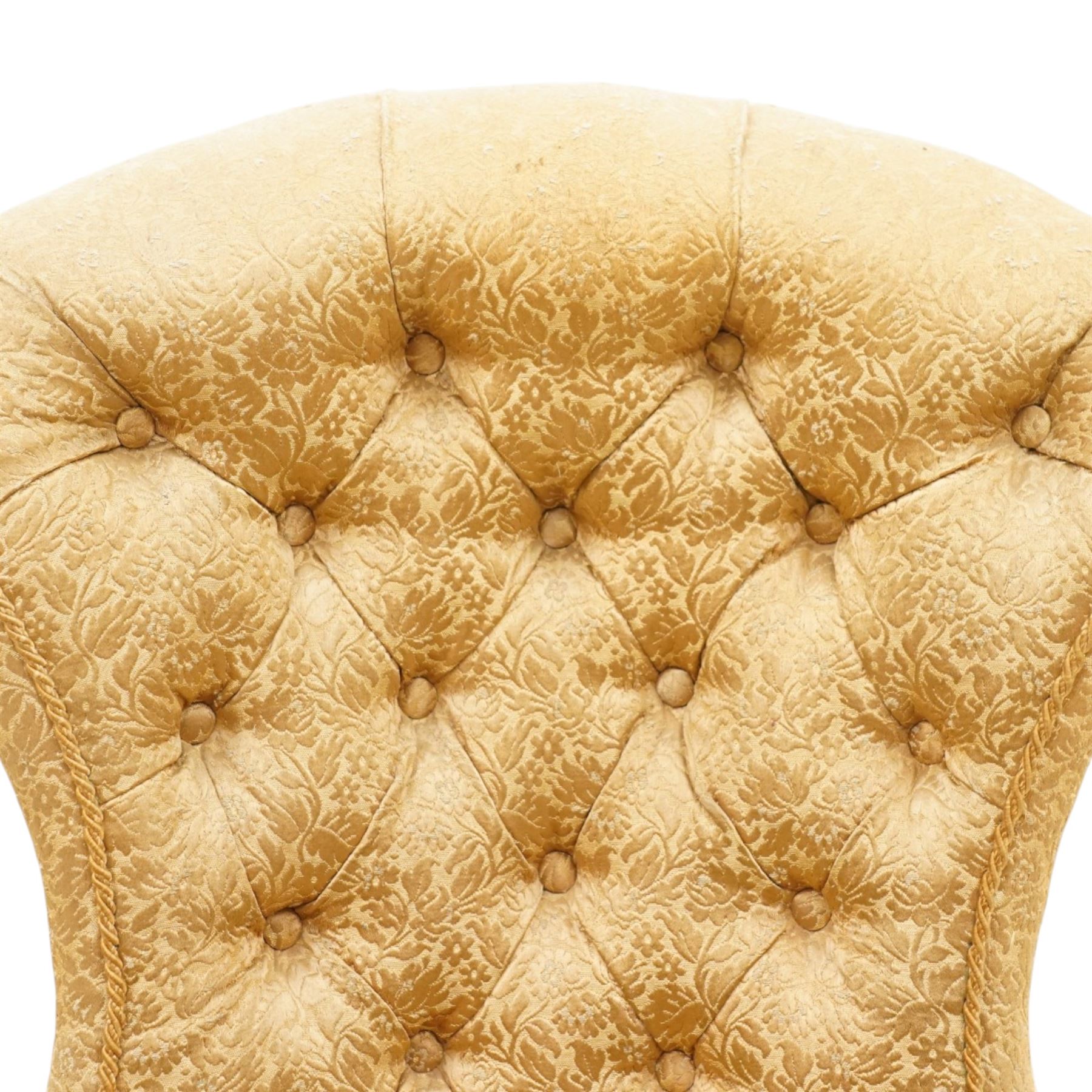 Victorian Aesthetic Movement walnut framed nursing chair, the fan back and sprung seat upholstered in buttoned foliate patterned gold damask fabric with fringing, raised on beaded tapering fluted supports with ceramic castors