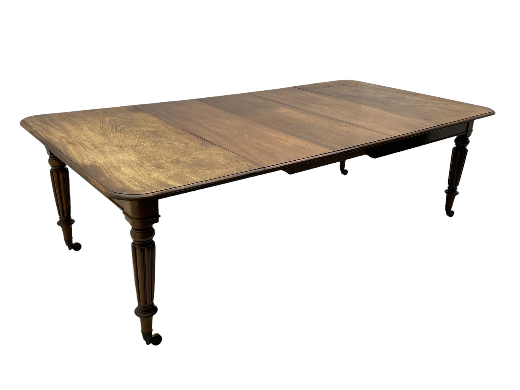Early 19th century figured mahogany extending dining table, the rectangular top with moulded edge and rounded corners, pull-out action with three additional leaves, raised on turned and lobe carved supports with brass cup castors