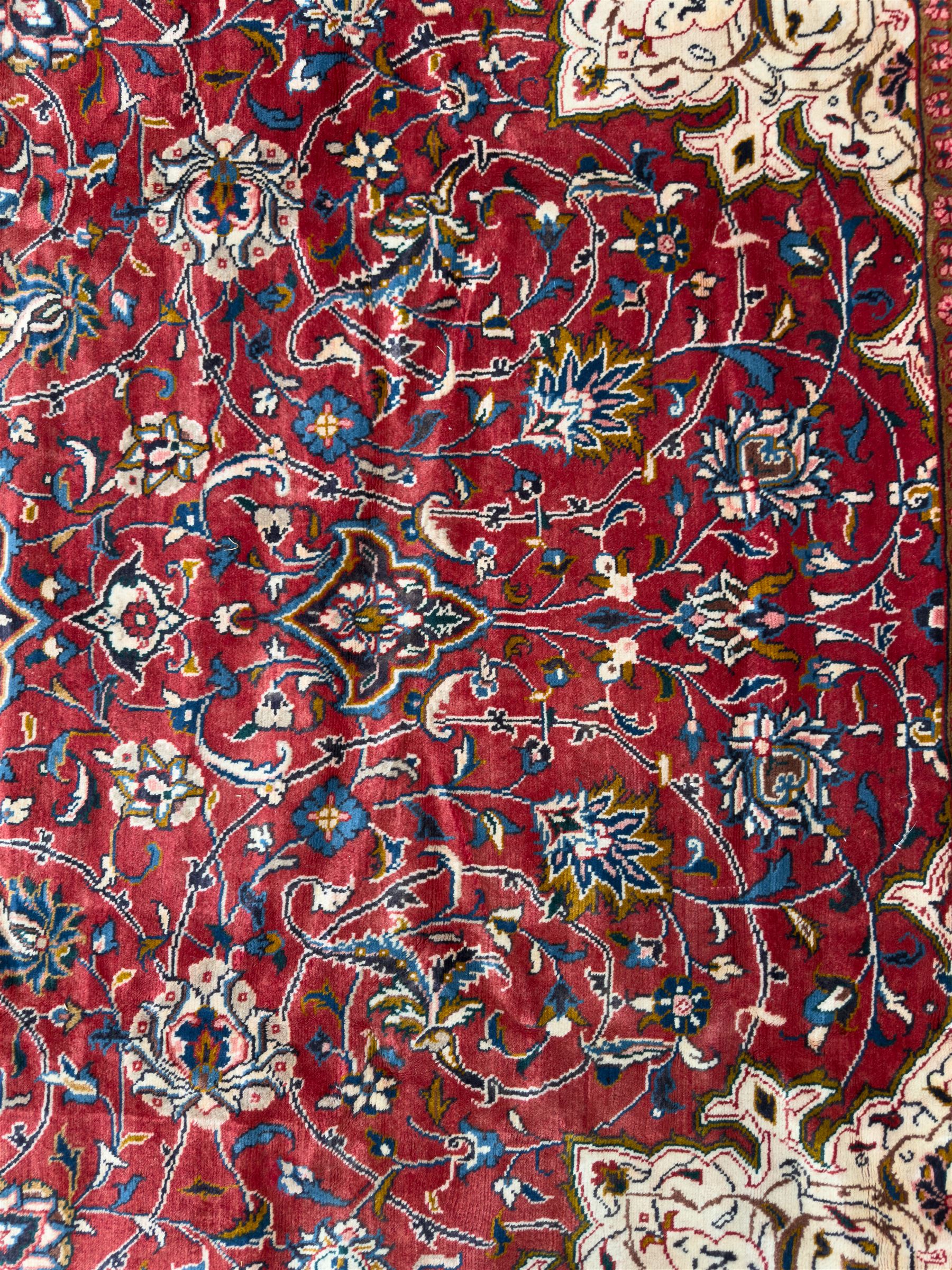 Northwestern Persian Lillihan hand-knotted carpet, madder red field with scrolling vines, rosettes, and palmettes around a central circular medallion in navy, ivory and ochre, and ivory ground spandrels within a navy border of stylized flowerheads and vines between multiple guard stripes 