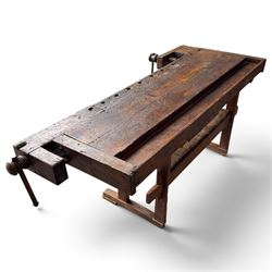Large early 20th century rustic stained reclaimed pine workbench, the substantial plank top with recessed tool well and two homemade wooden screw vices, above a single frieze drawer and slatted undertier, raised on trestle end supports