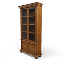 Pair of late 20th century Thai hardwood display cabinets, each with moulded cornice over twin glazed doors enclosing adjustable shelves, panelled cupboard doors below flanked by fluted columns, raised on bun feet