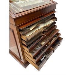 Edwardian mahogany artist's cabinet once belonging to the British artist Eli Marsden Wilson (1877-1965), raised panelled back mounted by carved brackets, sloped and hinged glazed lid enclosing paint holders and compartments, up-and-over panelled door revealing three slides, fitted with two banks of five graduating drawers with recessed brass handles, on skirted base.

Together with a quantity of artists' equipment and tools including paints, paintbrushes, charcoal, chalks, etc. and various prints relating to the life of the artist, including Quaker anti-war posters, Victorian Stevengraphs, and various chromolithographs 

Provenance: Removed from the studio of Eli Marsden Wilson. The cabinet comes to us for sale through family descent. The vendor is descendant of Marsden. Many further etchings removed from the cabinet are being sold in the Spring Art Sale, Friday 15th March 2024, Lots 265-271.

Notes: born in Ossett, Eli Marsden Wilson was the only son of Alfred Wilson, a foreman beamer, and Emma Marsden, and had five sisters. After studying at Wakefield College of Art, he moved to the Royal College of Art in London, where he became a pupil of Sir Frank Short. He had his first exhibit at the Royal Academy in 1905, the same year he married fellow artist Hilda Mary Pemberton.

A Quaker, vegetarian, and pacifist, he was a conscientious objector in World War I and as such was imprisoned in 1917 for two years. In September 1922 he was commissioned by Princess Marie Louise to produce miniature etchings for Queen Mary's Dolls' House at Windsor Castle; two such etchings are being sold in the Spring Art Sale, Friday 15th March 2024, Lot 265.