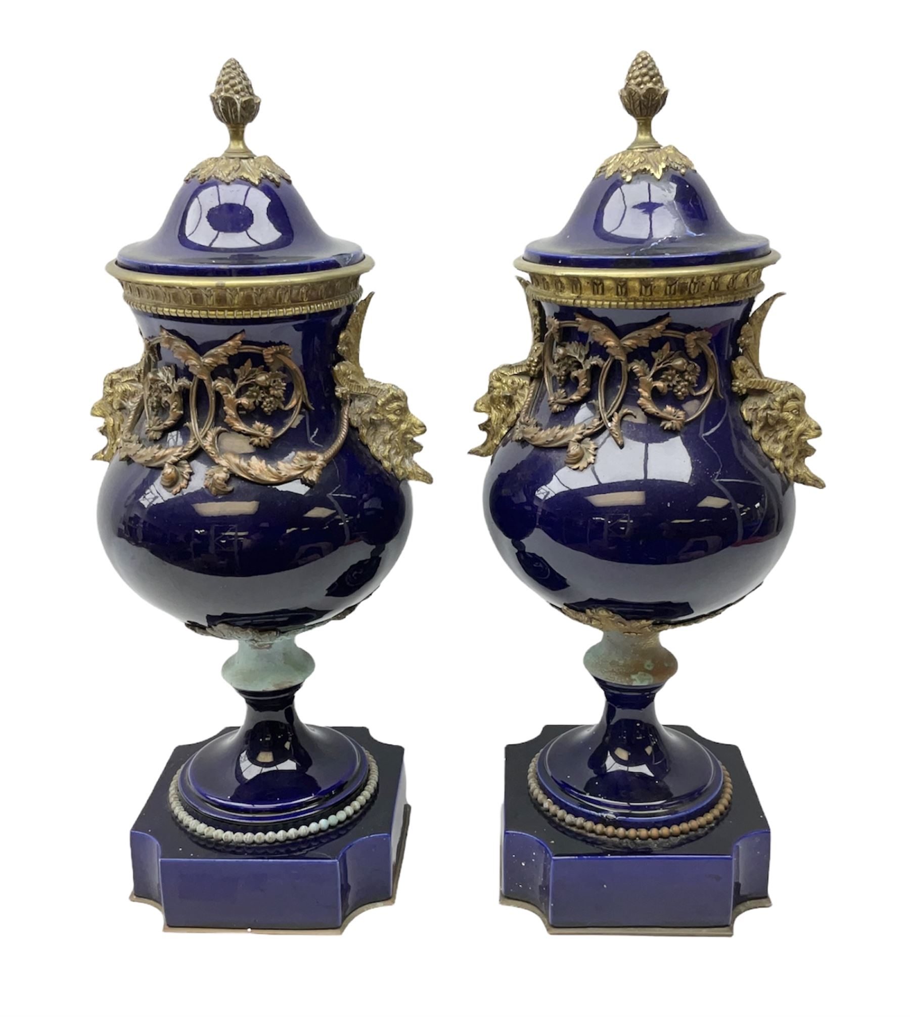 Pair of French large cobalt blue lidded urns, probably 19th century, the body decorated with ormolu ram's heads and ornate foliate design, the domed cover with brass berry finial, raised upon pedestal base with beaded decoration upon shaped plinth, H52cm