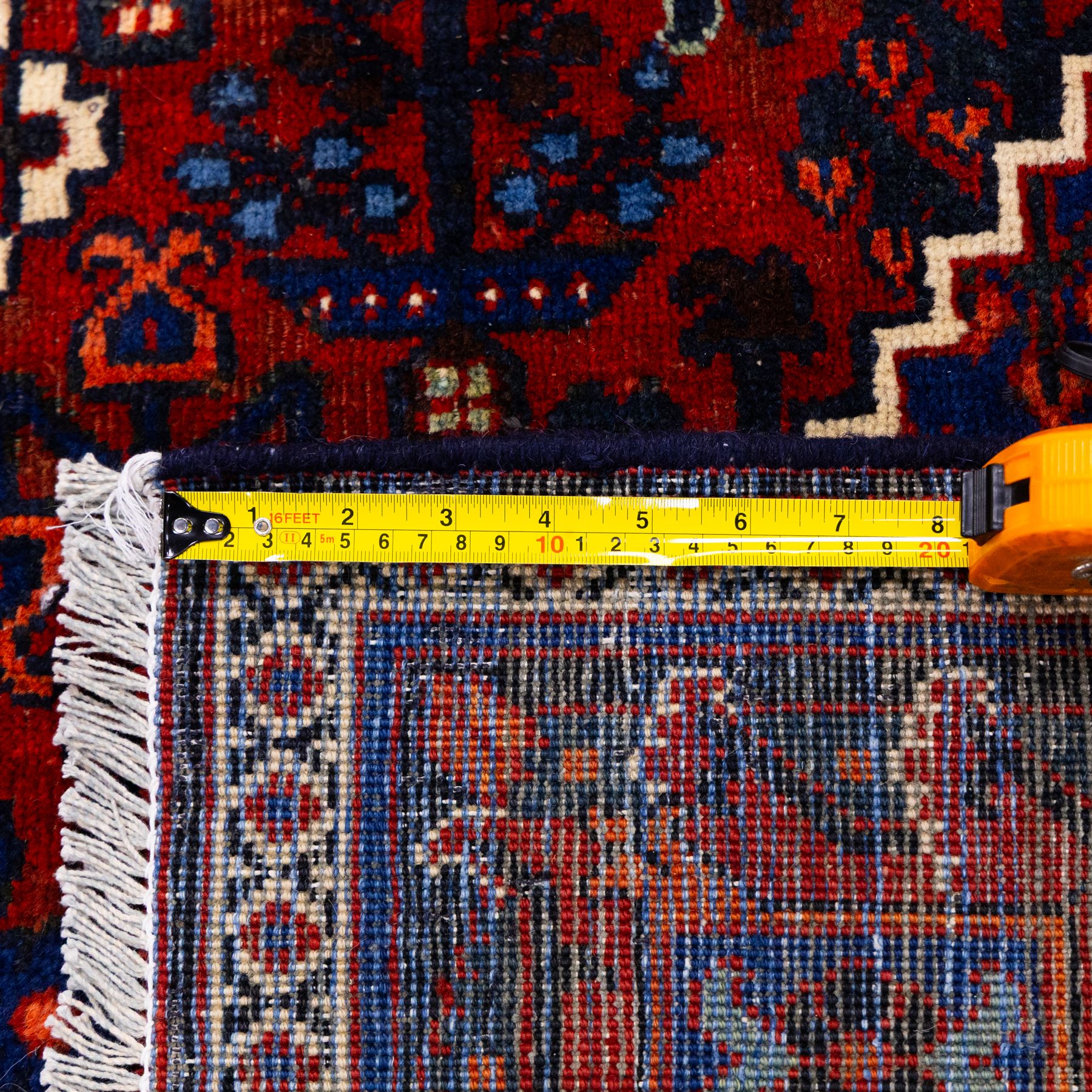 Central Persian Joshagen hand-knotted carpet, madder-red field with a central stepped lozenge medallion and densely filled with stylized geometric floral and tree motifs arranged in a repeating lattice enclosed by indigo spandrels and a broad navy border of angular palmette and vine ornament, flanked by multiple guard stripes, cotton fringe ends 