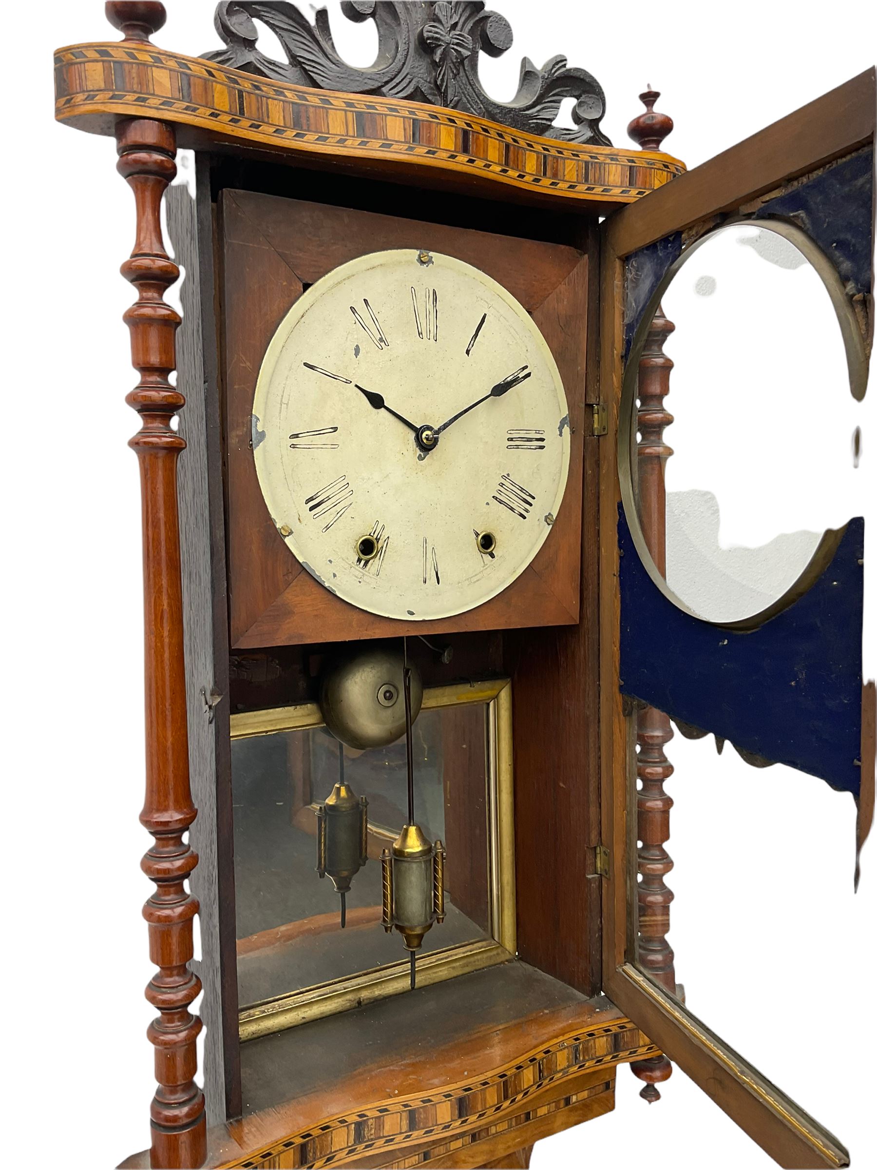 A late 19th century spring driven American Eight-day wall clock, striking the hours on a bell, in a parquetry case with contrasting oak, maple, walnut, and other hardwoods, with a flat top, carved cresting and finials rectangular glazed door flanked by finely turned pilasters, with a painted dial with roman numerals and minute track, steel spade hands and faux mercury pendulum reflected in a rear case mirror.   


