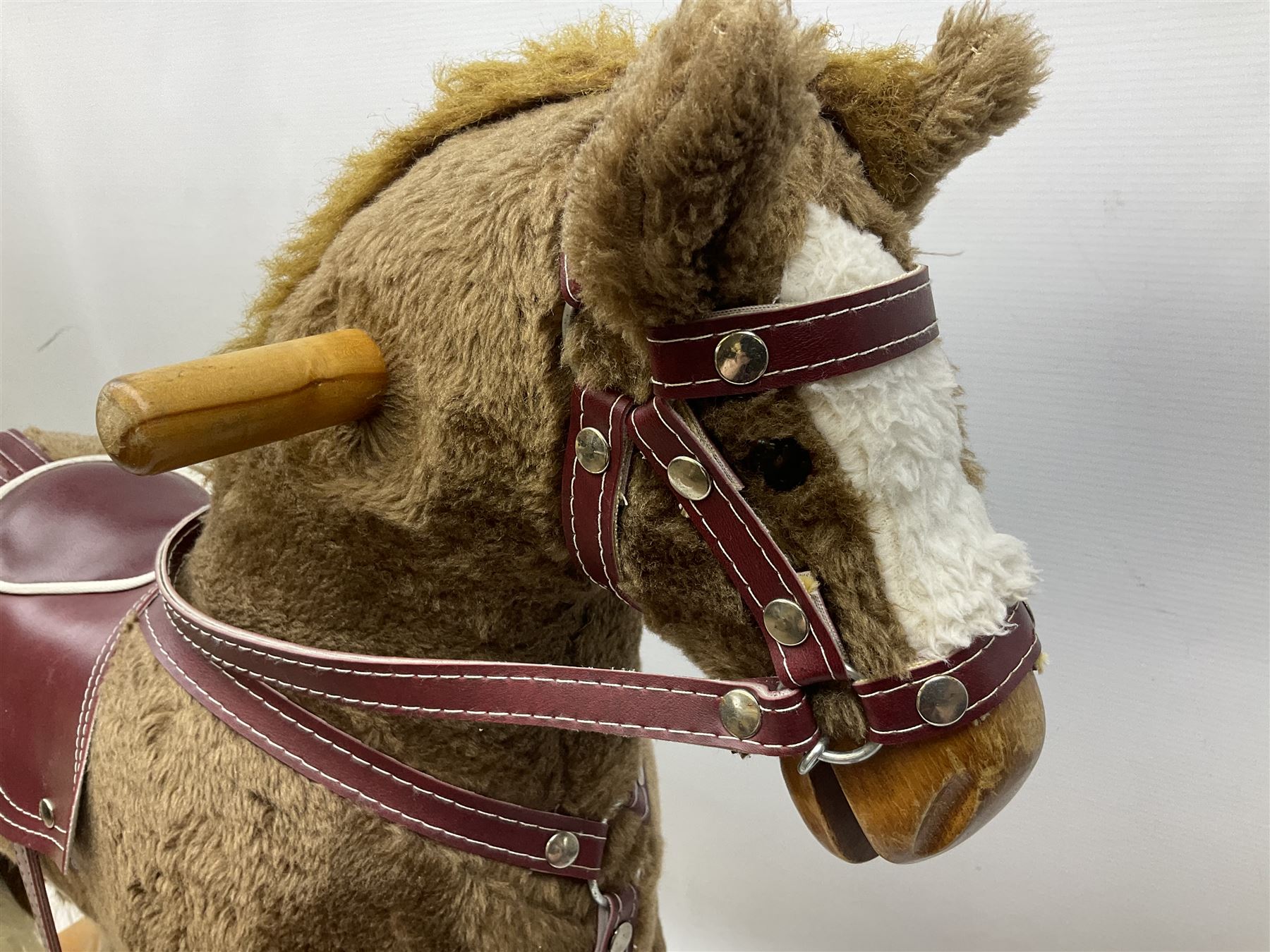 Modern plush covered rocking horse with inset eyes, simulated leather bridle and saddle with metal stirrups, on curving wooden rockers L94cm H64cm