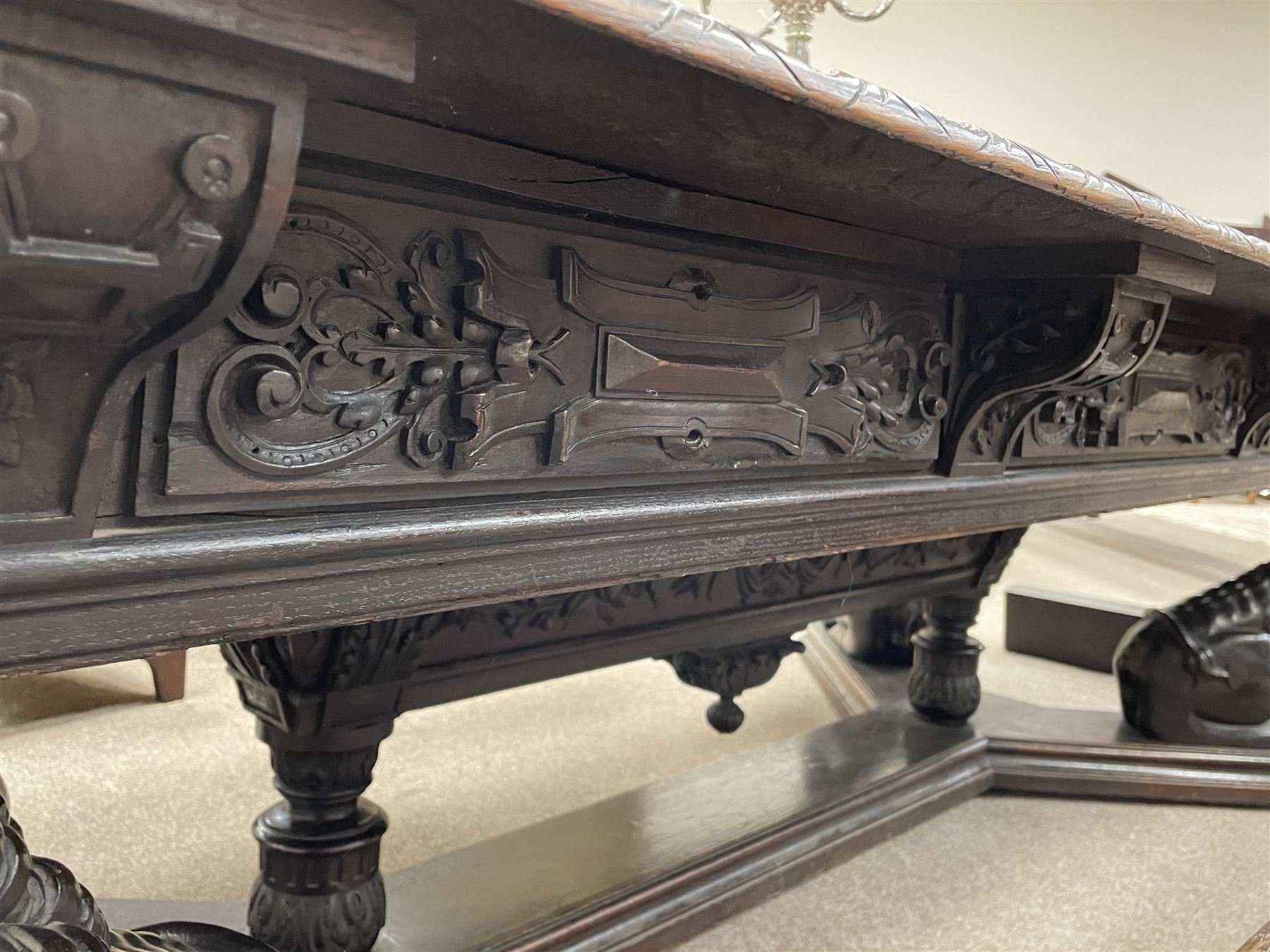 Large 19th century carved oak library table, the rectangular top with lunette carved edge over cartouche panelled and carved  scroll frieze, the central tapering rectangular support relief carved with masks and garlands, on four carved seated lion supports at each corner, on flat angular stretcher with recessed castors stamped ‘Bartholomew & Fletcher, London’
