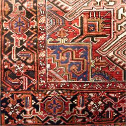 North West Persian Heriz hand-knotted carpet, madder red field, with a large angular stepped central medallion with serrated outlines, flanked by bold stylized palmettes, hooked leaves and geometric devices, spandrels similarly decorated within a wide geometric main border featuring angular floral motifs, enclosed by multiple guard borders in madder red, indigo blue, ivory, olive green and soft ochre, with cotton fringe ends 