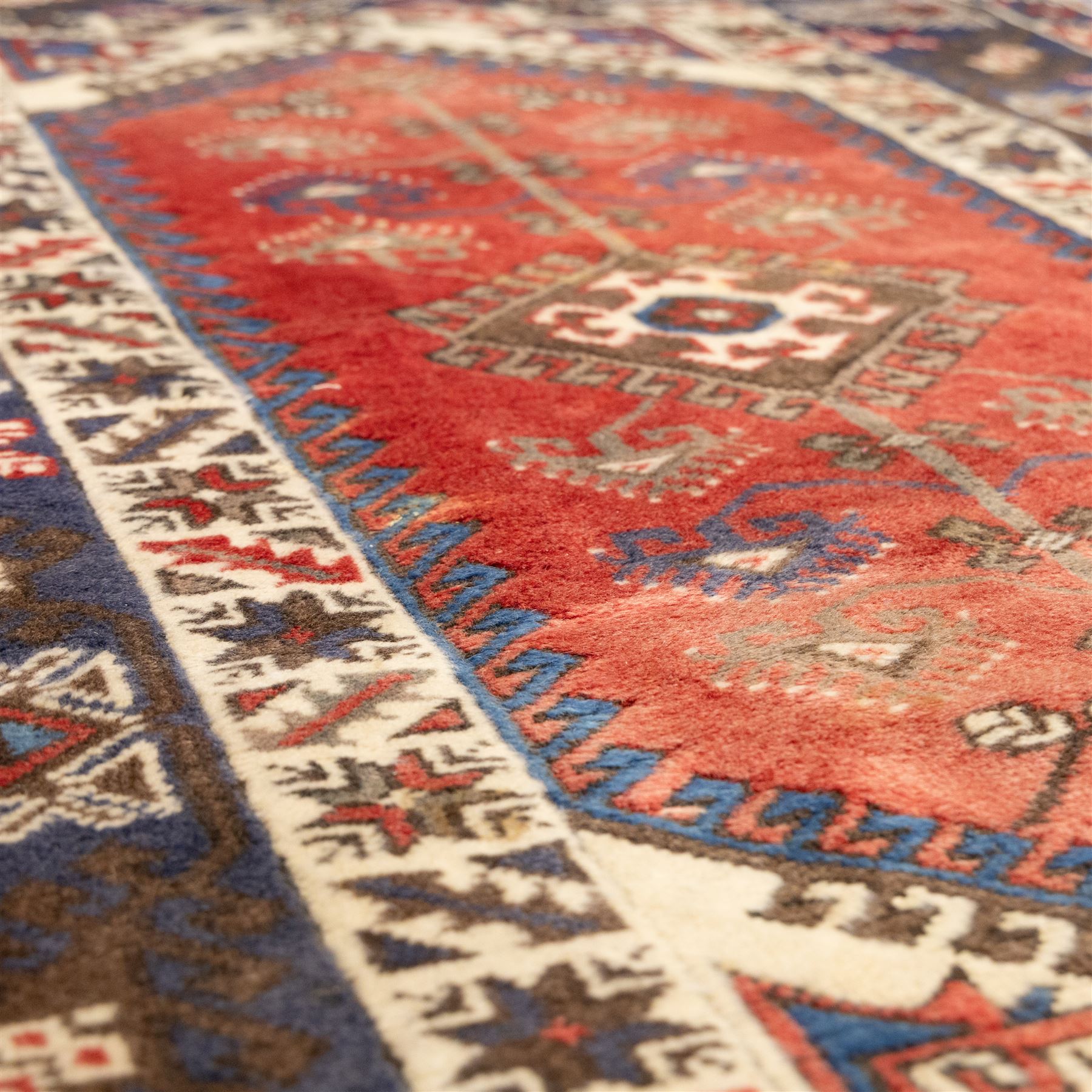 Caucasian Shirvan hand-knotted rug, red madder field with hooked lozenge medallions and stylized motifs, framed by ivory stepped spandrels and multiple geometric borders in indigo brown and ivory, with serrated palmettes and angular devices 