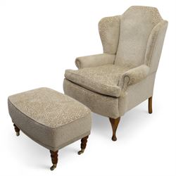 Late 20th century wingback armchair and matching footstool, upholstered in beige embossed fabric with brass stud edging, on cabriole legs and splayed rear legs, together with a matching footstool on turned supports terminating in brass castors (Stool H 42cm, W 75cm, D 47cm)