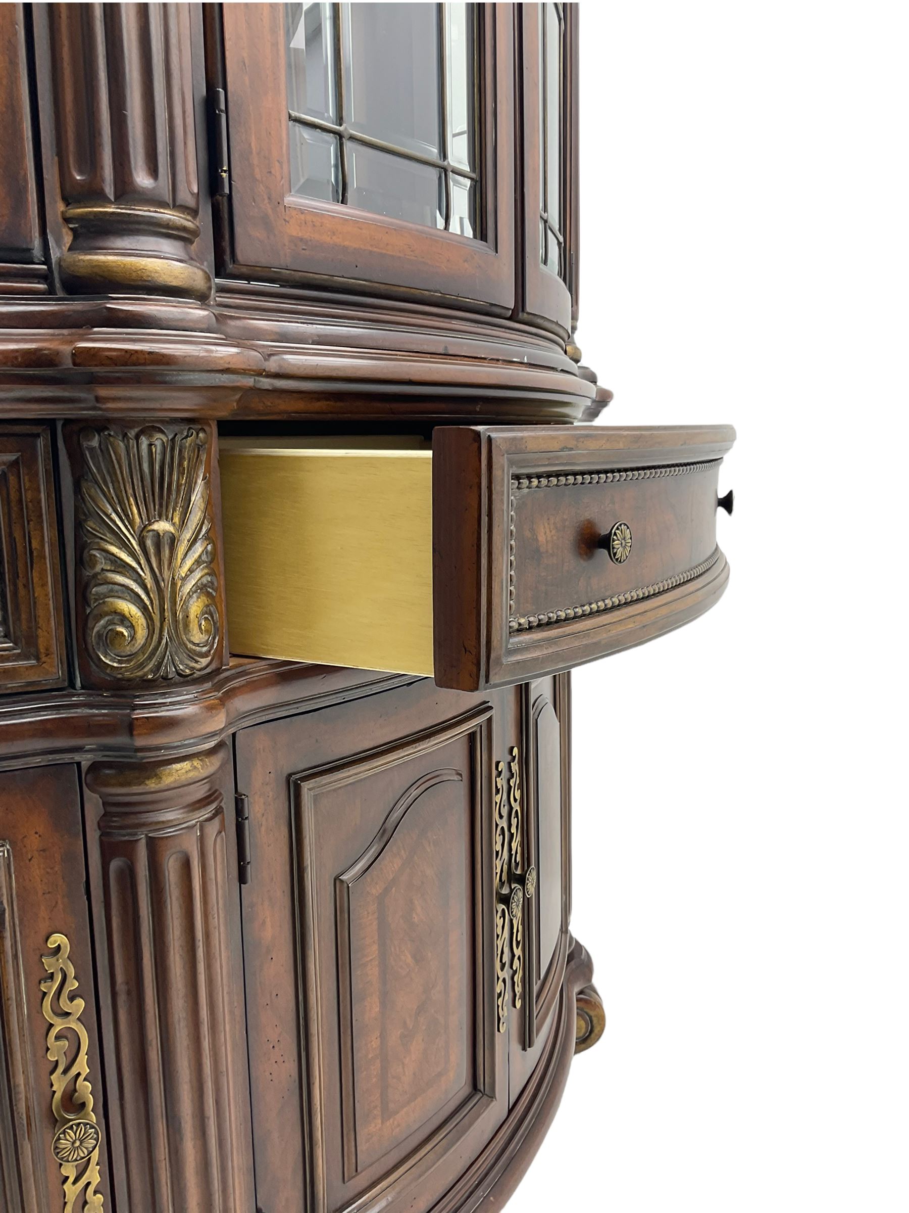  Kevin Charles American walnut demi lune display cabinet with illuminated interior, projecting cornice, two bevel edge glazed doors enclosing two adjustable shelves above single drawer and four cupboard doors with wine rack, carved scrolling supports