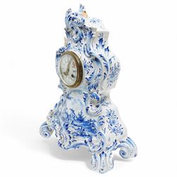 19th century delft blue and white Rococo style 8-day mantle clock, with a scrolling case and floral decoration, depiction of a courting couple in 18th century dress to the front and a contrasting scene of sailing ships on a lake to the rear, with a late 19th-century French twin train movement, enamel dial with Roman numerals, five minute Arabic's and gilt Louis XVI hands within a glazed cast bezel, with a rack striking movement sounding the hours and half-hours on a bell. No pendulum or key.  