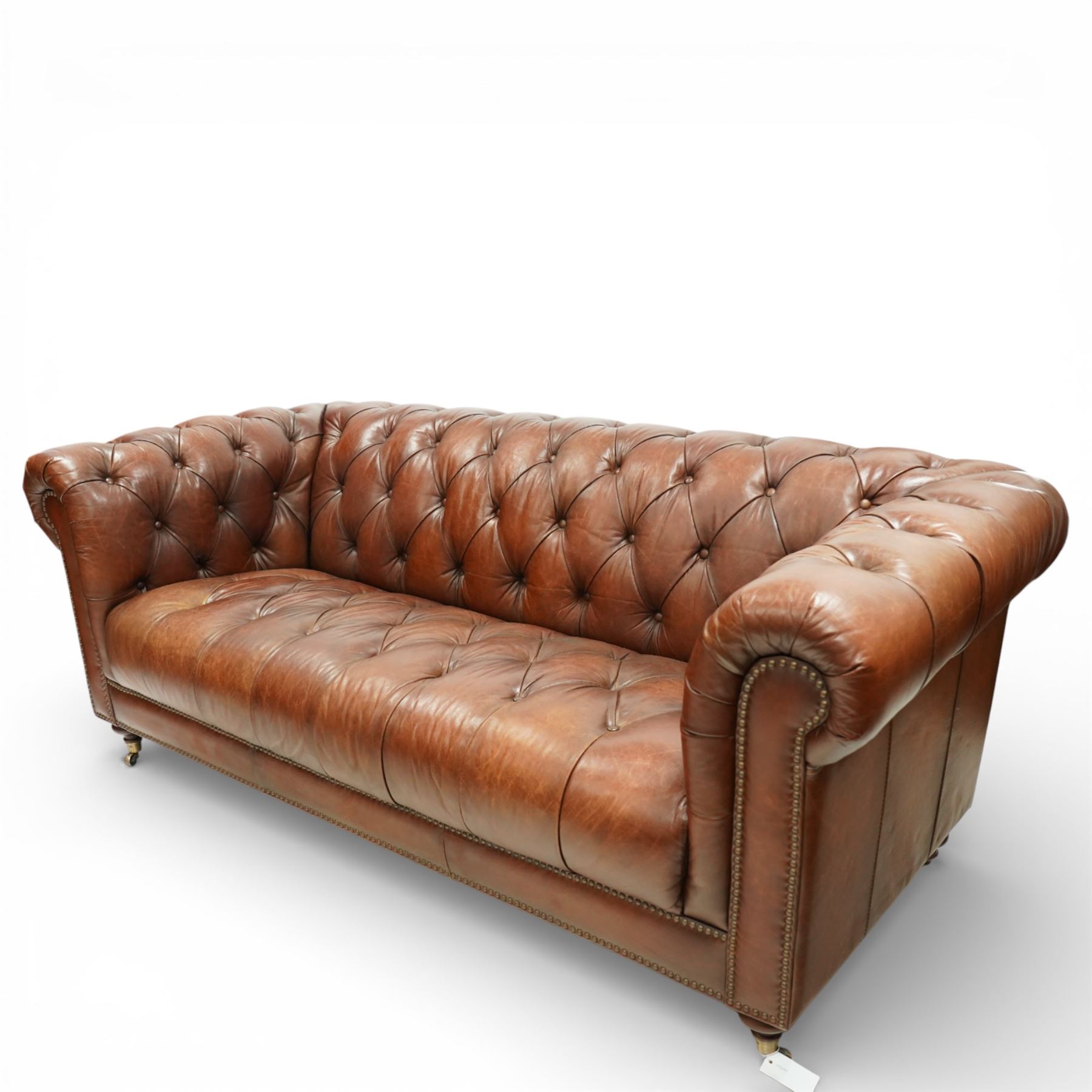 Ullswater - late 20th century brown leather chesterfield sofa, deep button tufted back, arms and seat, classic rolled arm form with studded borders to the arms and base, raised on turned feet with castors