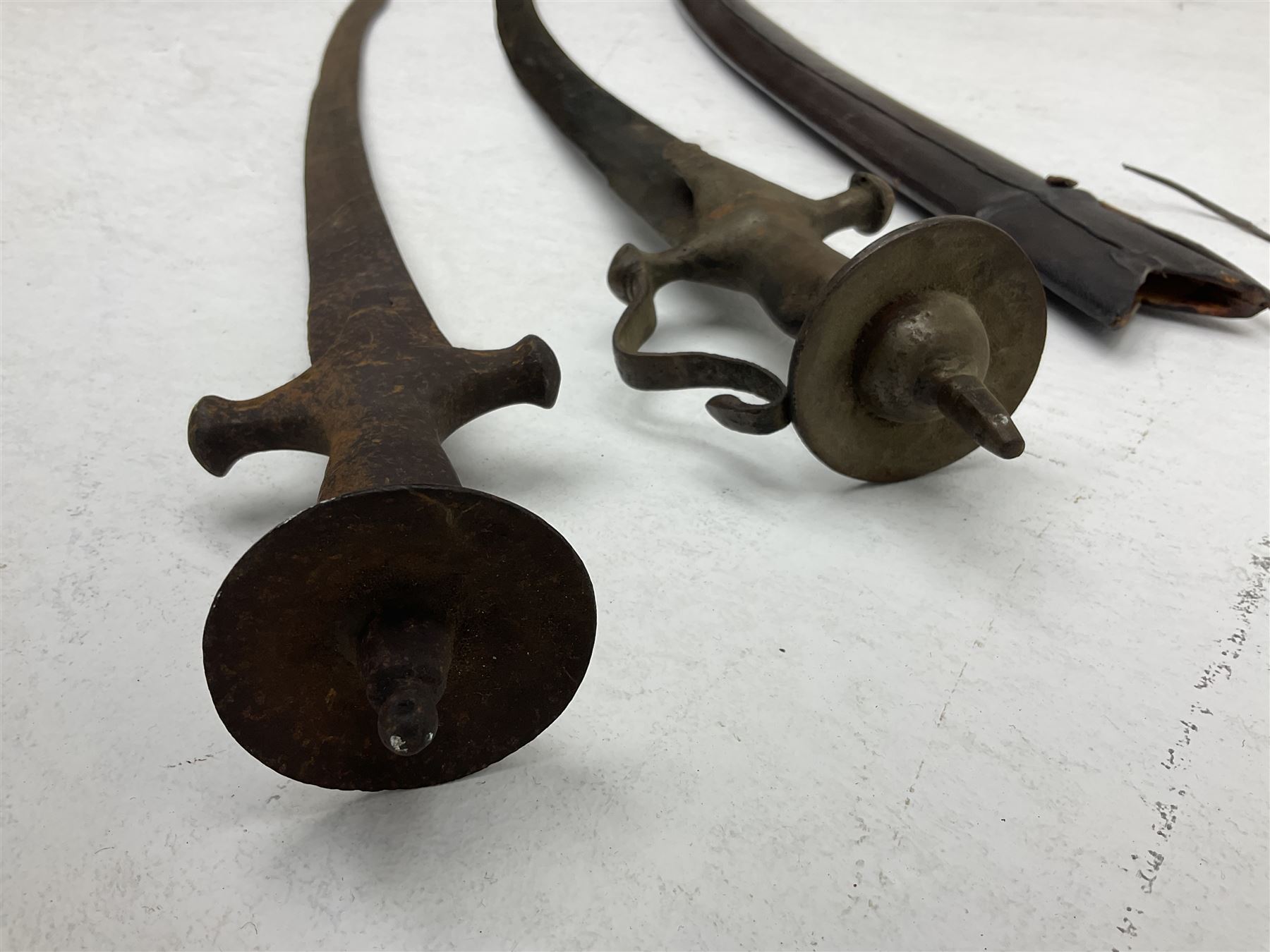 Late 19th/early 20th century Indian Tulwar sword with 81cm plain curving steel blade and iron hilt with extended langets, knucklebow and spiked pommel; in leather covered scabbard L100cm overall; and another Tulwar lacking scabbard in almost relic condition (2)