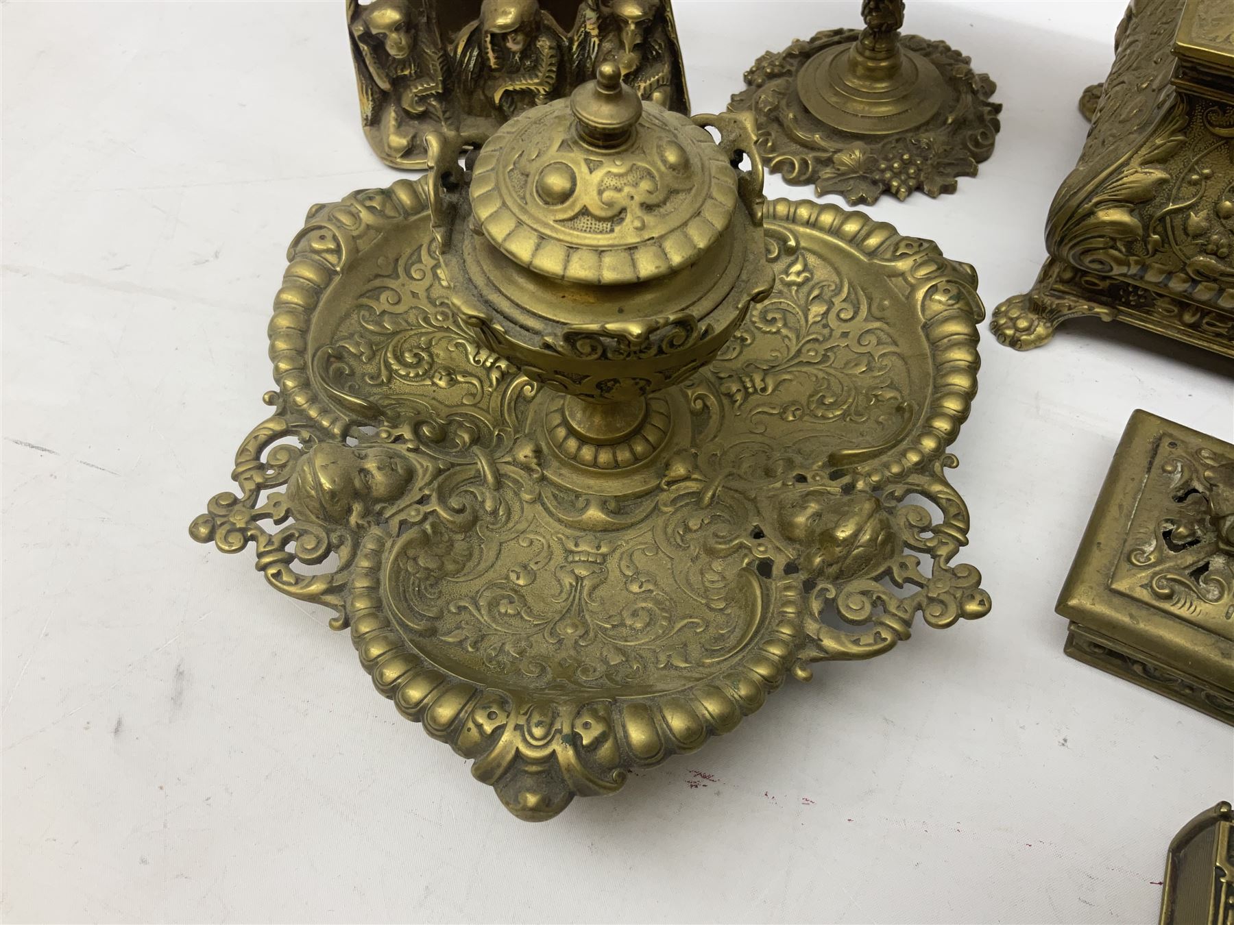 Collection of victorian and later brass desk accessories, to include a letter holder with cherub design, ink well of square form with hinged lid, brass table bell, brass casket with relief decoration, etc  