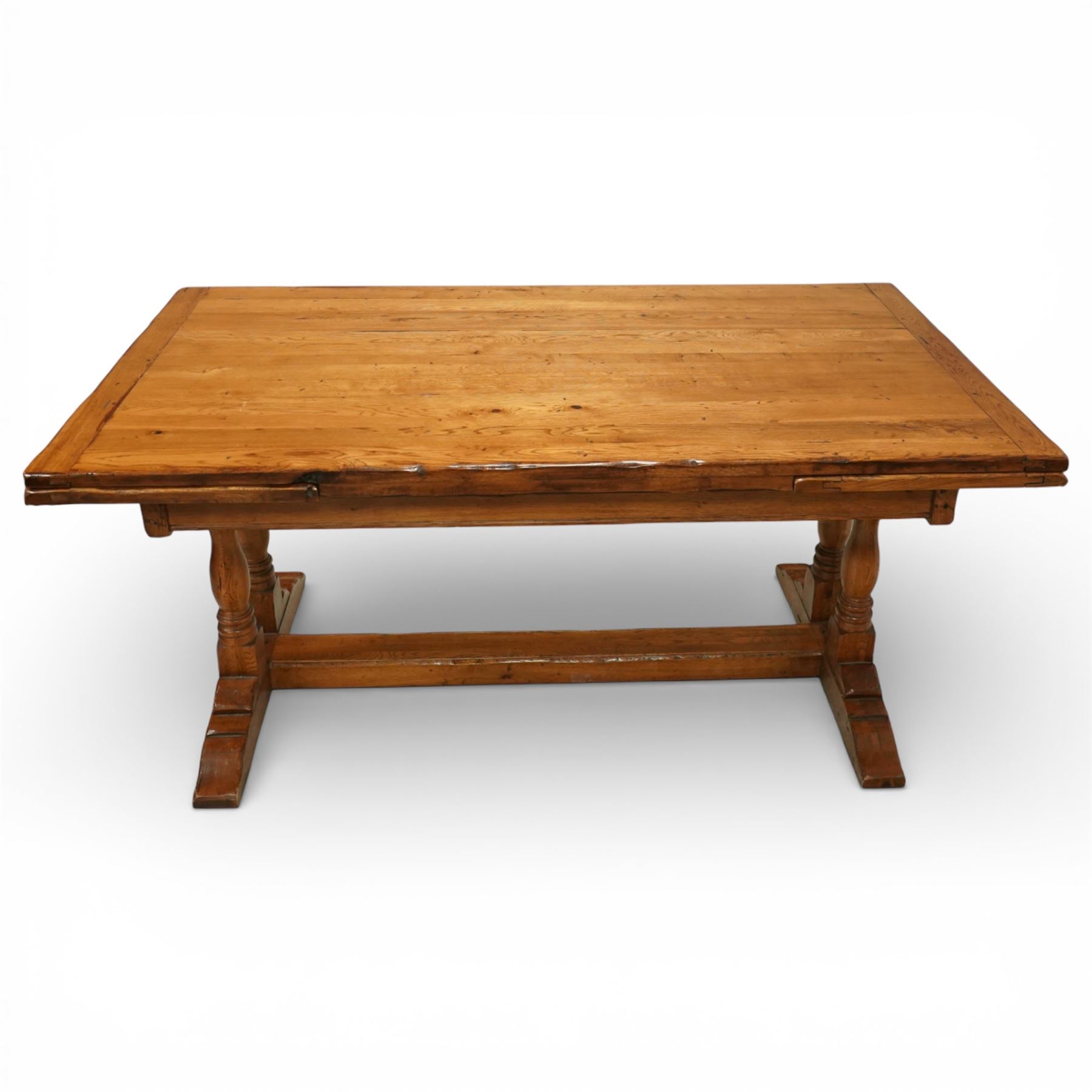 Late 20th century light oak extending refectory table, in the manner of Titchmarsh & Goodwin, rectangular plank top with cleated ends and two draw leaves extending to 260cm, supported on turned end supports united by a stretcher, raised on block feet