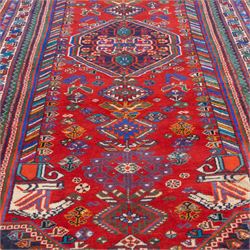 South West Persian Qashqai hand-knotted runner, madder red field  with central vertical succession of stepped lozenge medallions enclosing angular tribal devices and stylized floral motifs, principal medallion in deep indigo with ivory and sky blue highlights, field densely scattered with small geometric ornaments, hooked elements and zoomorphic forms, triangular indigo spandrels enclosed within multiple narrow guard stripes and principal border, with cotton fringe ends 
