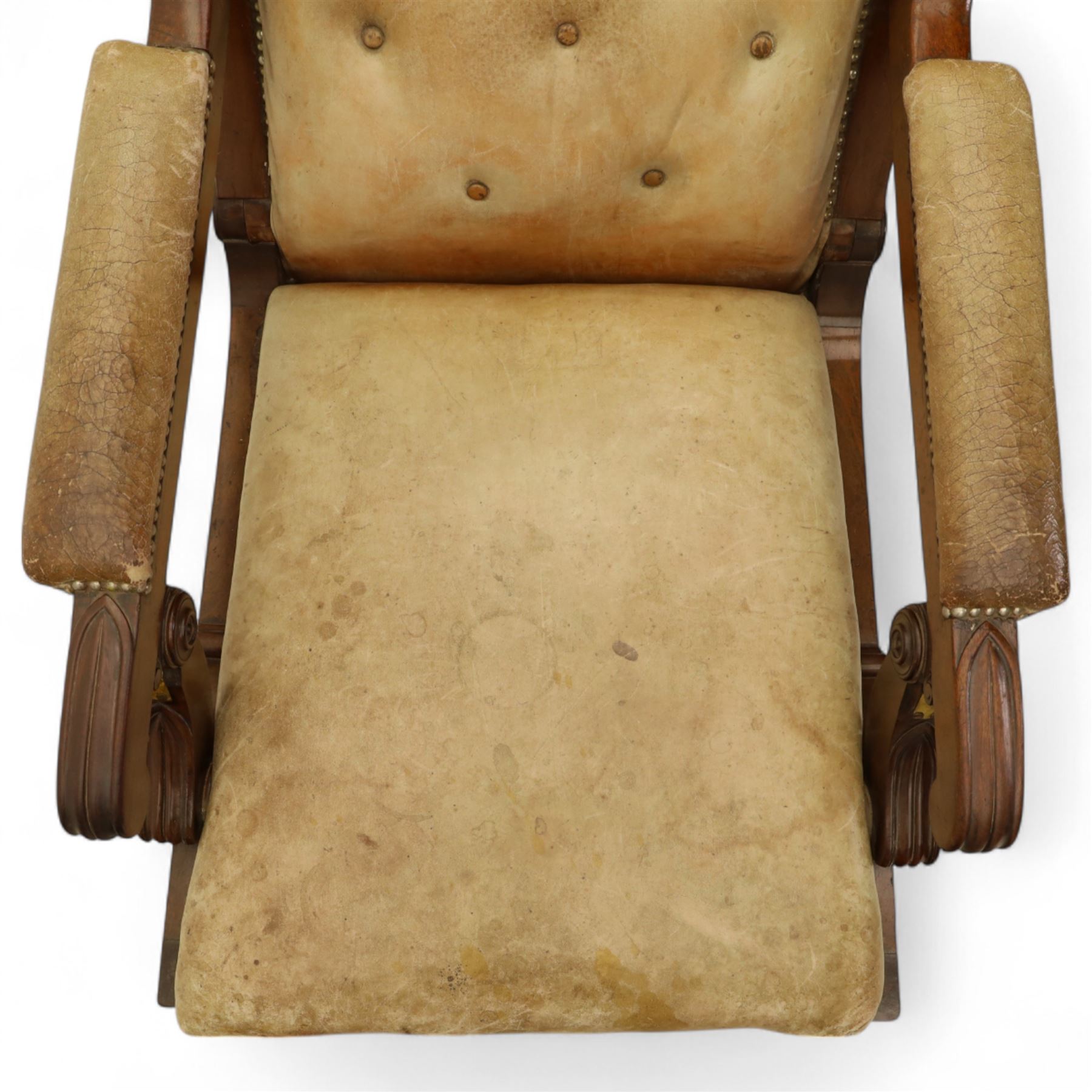 William IV mahogany gentleman's library reclining armchair, leather button upholstered and brass-studded back and seat, above leather-covered arms terminating with carved roundels and foliate scroll-carved ends, underside with brass mechanical trigger reclining lever, the apron with retractable foot rest, supported on lappet carved and turned legs with brass castors, circa 1835