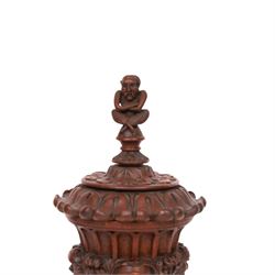 Carved wooden urn. decorated in relief with carved faces within foliage, with a Satyr finial, H25cm 