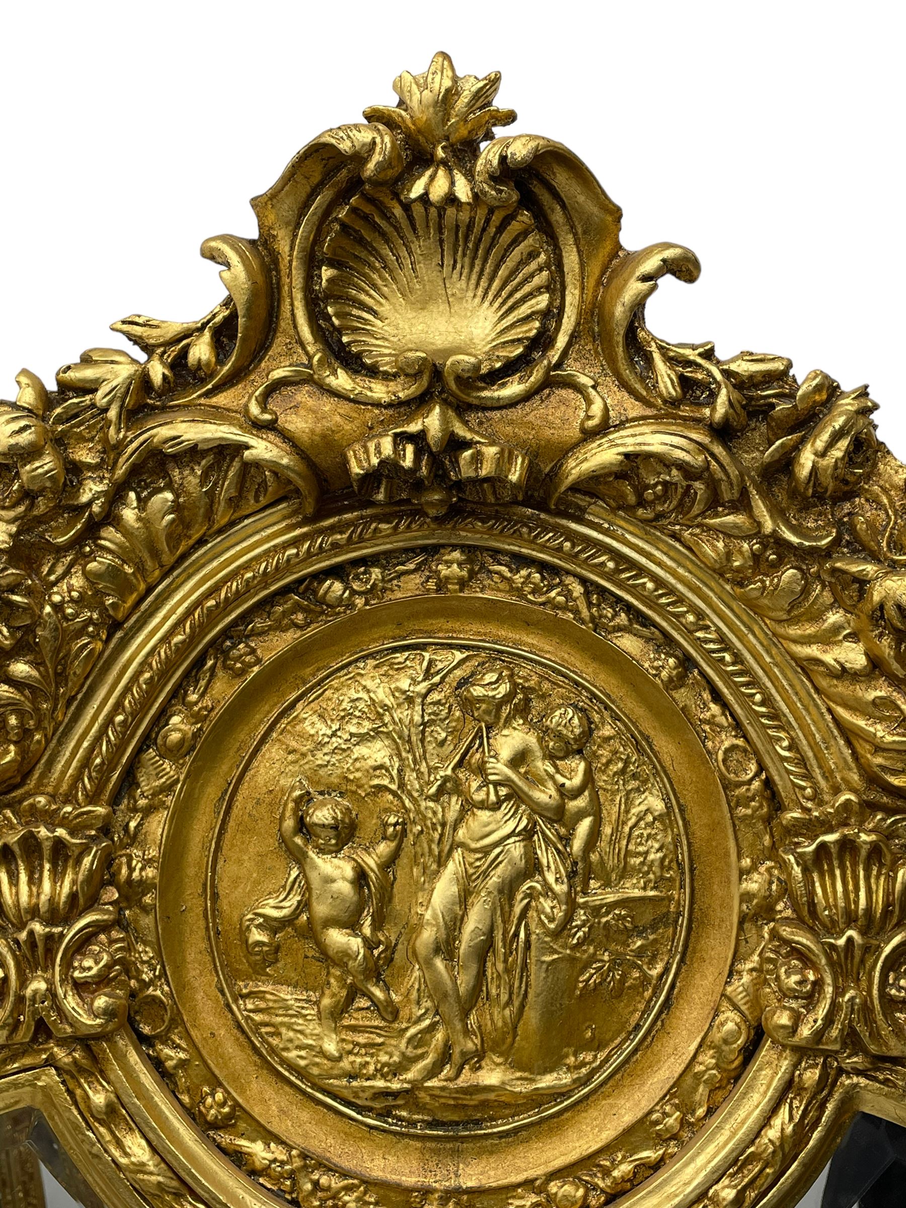 Large Italian Baroque design gilt wall mirror, the shell pediment over circular panel depicting classical female flute player with dancing putto within a tree landscape, the stepped arched upper frame surmounted by musical instrument playing putto and trailing flower heads, central bevelled mirror plate surrounded by plain segmented mirror plates, acanthus leaf moulded outer frame and foliate moulded inner slip