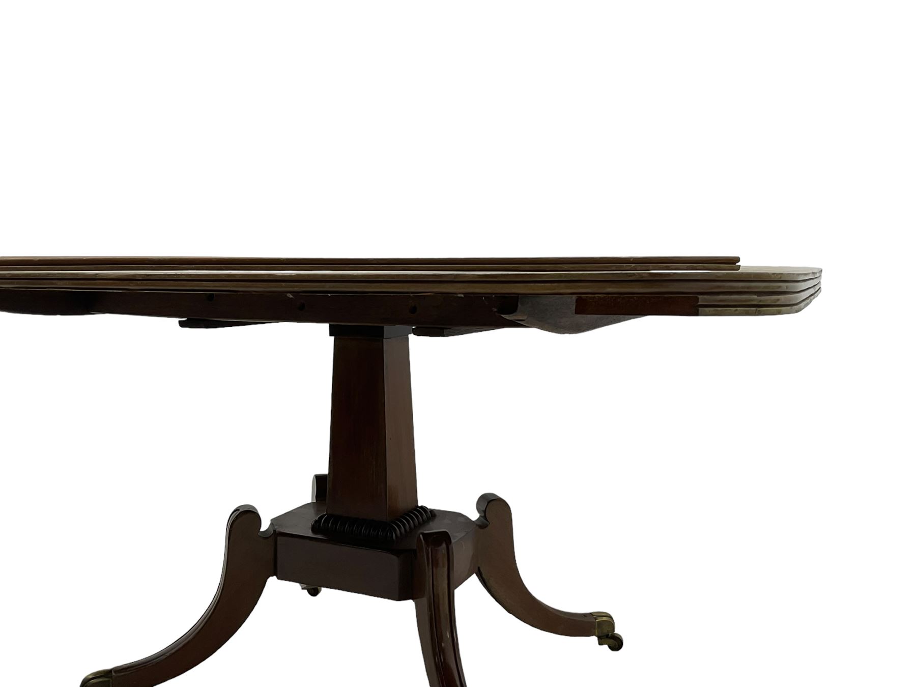 Regency mahogany dining table, rectangular top with rounded corners and reeded edge, raised on square pedestal with platform, terminating to sabre supports with brass cups and castors