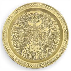 20th century Eastern brass charger topped table, the circular brass trap chased with an elephant, palm tress and flowering vines, supported upon a folding stand with six turned legs with inlaid detail, united by turned supports