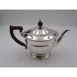 1930's silver three piece tea service, comprising teapot with wooden handle and finial, and engraved dedication to body, twin handled sugar bowl, and milk jug, each of part faceted form with gadrooned rim and upon spreading circular foot, hallmarked Adie Brothers Ltd, Birmingham 1931, approximate gross weight 18.93 ozt (588.8 grams)