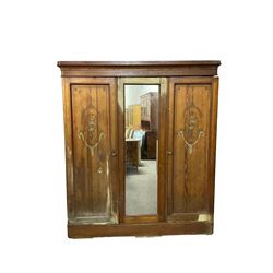 Late 19th century Arts and Crafts pitch pine triple wardrobe, shaped projecting cornice, central door with rectangular mirror plate, flanked by two panelled doors with floral foliate painted designs with trailing garlands, raised on plinth base, interior fitted with four sliding open shelves over four drawers