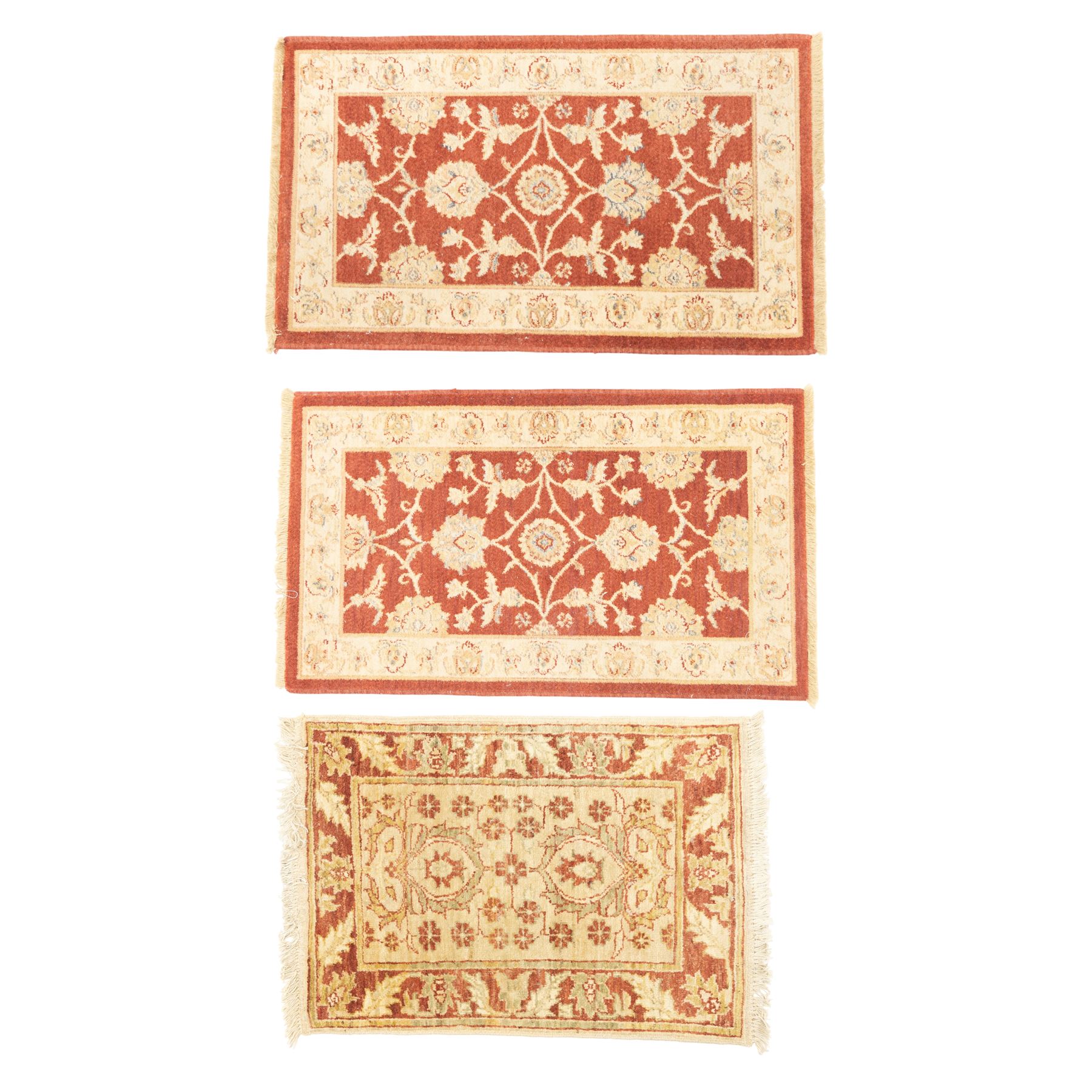 Lot of three Indo-Ziegler style wool rugs, comprising one with central floral medallion and palmette border, and two matching examples with scrolling vine and flowerhead motifs on a deep red field, each with decorative border in soft gold tones (60cm x 85cm) (65cm x 115cm)