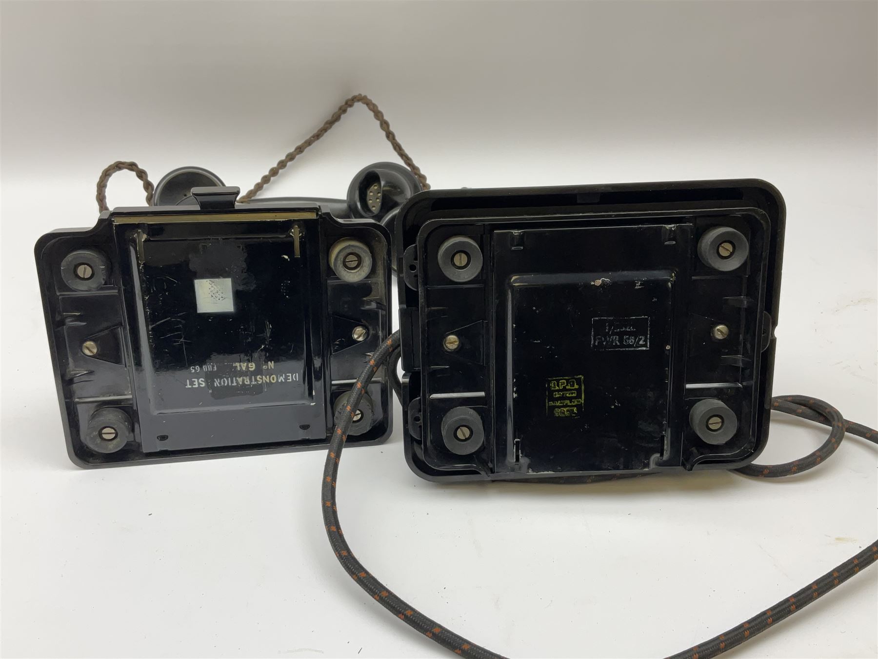 Two black Bakelite telephones of pyramid form with rotary dials, comprising The Telephone Demonstration Set model. 6al with base drawer and light bulb, and another larger with G.P.O FWR 58/2 stamped marks beneath, largest H18cm W20cm D16cm