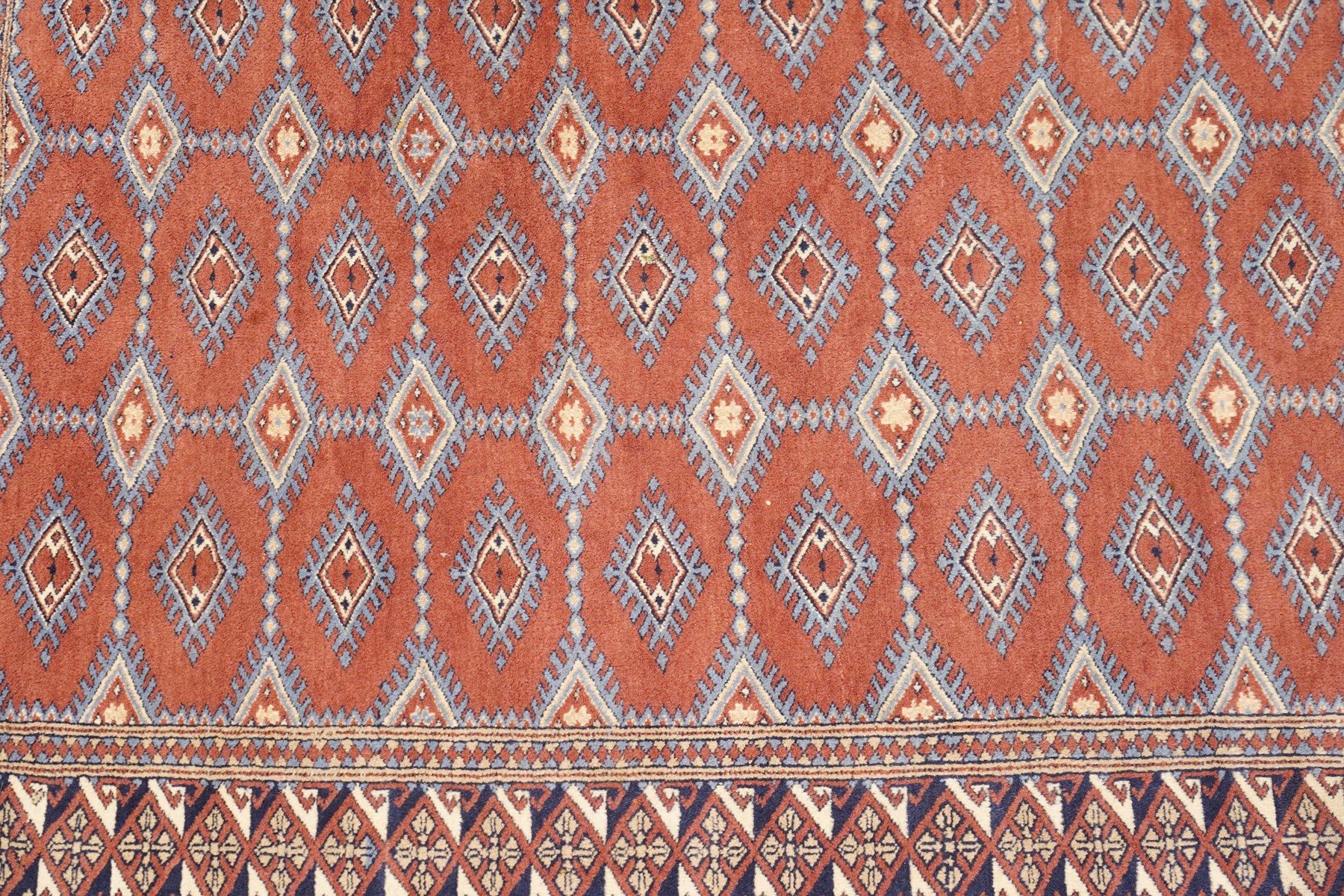 Afghan Turkoman crimson ground rug decorated with twin rows of hooked geometric guls within broad compartmented geometric borders (125cm x 201cm); Afghan Bokhara rug with repeated octagonal guls on a terracotta ground, enclosed by multiple geometric borders and patterned elem panels (120cm x 192cm) (2)