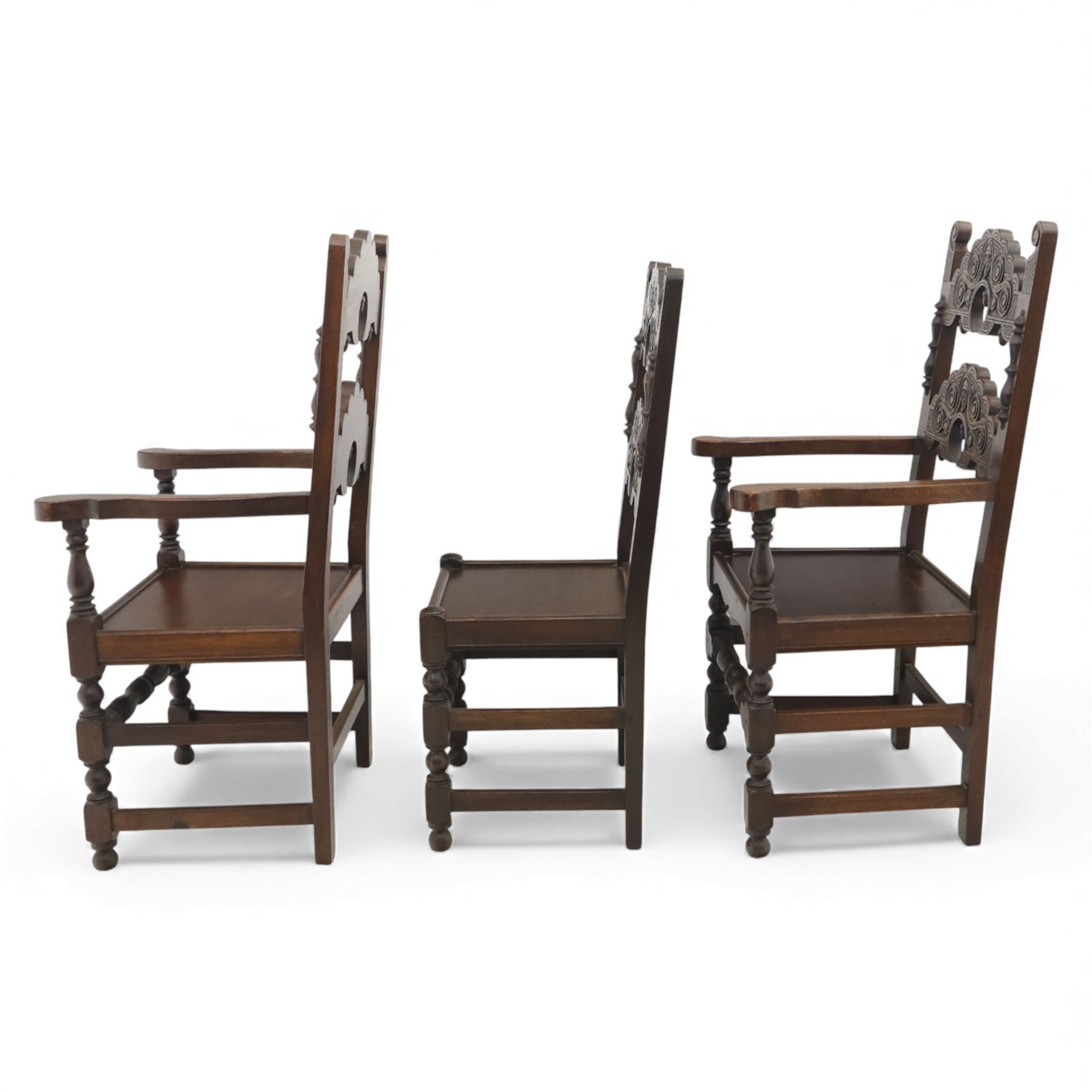 Early 20th century set of seven Jacobean Revival oak chairs, comprising pair of cavers and five chairs, each with carved mask and scroll decoration to the crest and and back rail, plain oak seat, upon turned front legs and block rear legs with conforming stretchers