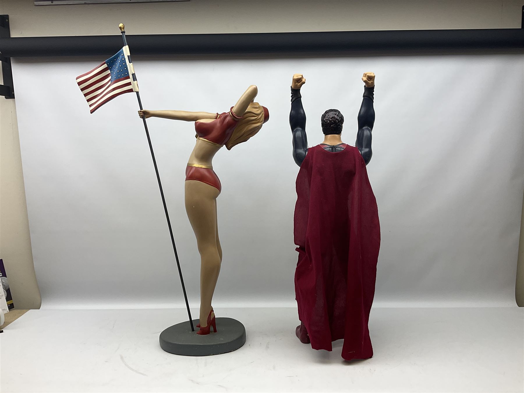 Composite Superman with cape, together with a composite female statue holding the American flag, tallest example H103cm