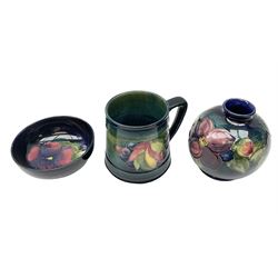 Three pieces of Moorcroft pottery, comprising squat baluster form vase in the Clematis pattern, upon a dark blue and green ground, bowl in the Pansy pattern upon a blue ground and a tapering mug in the Leaf and Berry pattern upon a dark green ground, each with printed marks beneath, tallest example H11cm
