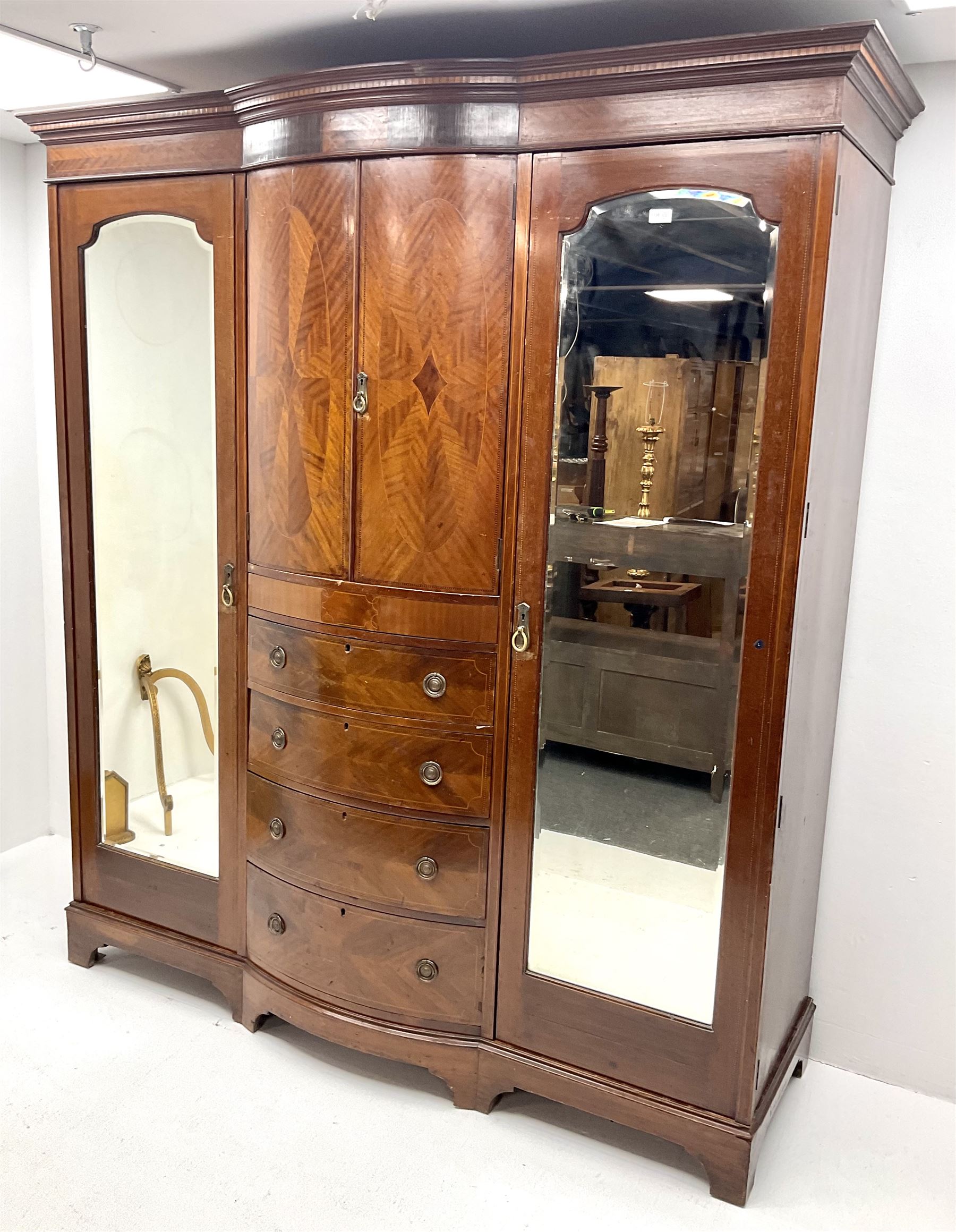 Edwardian inlaid mahogany triple wardrobe, bow front centre with two cupboards above four graduating drawers flanked by two bevel edged mirror doors, shaped platform base 