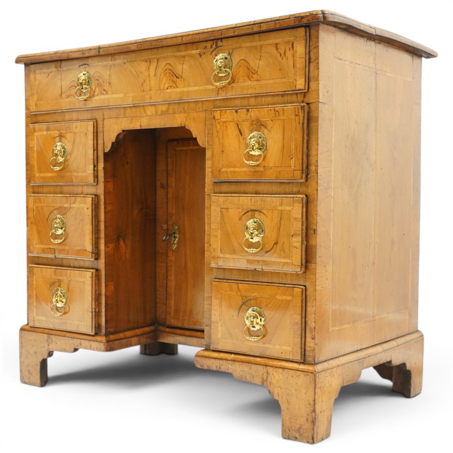 George III figured and burr walnut kneehole desk, the shaped rectangular top with feather and crossbanding surrounded by a moulded edge, fitted with single frieze drawer over three graduating drawers to each side, flanking a central recessed cupboard, lower moulded edge on bracket feet
Provenance: Kirkham Hall