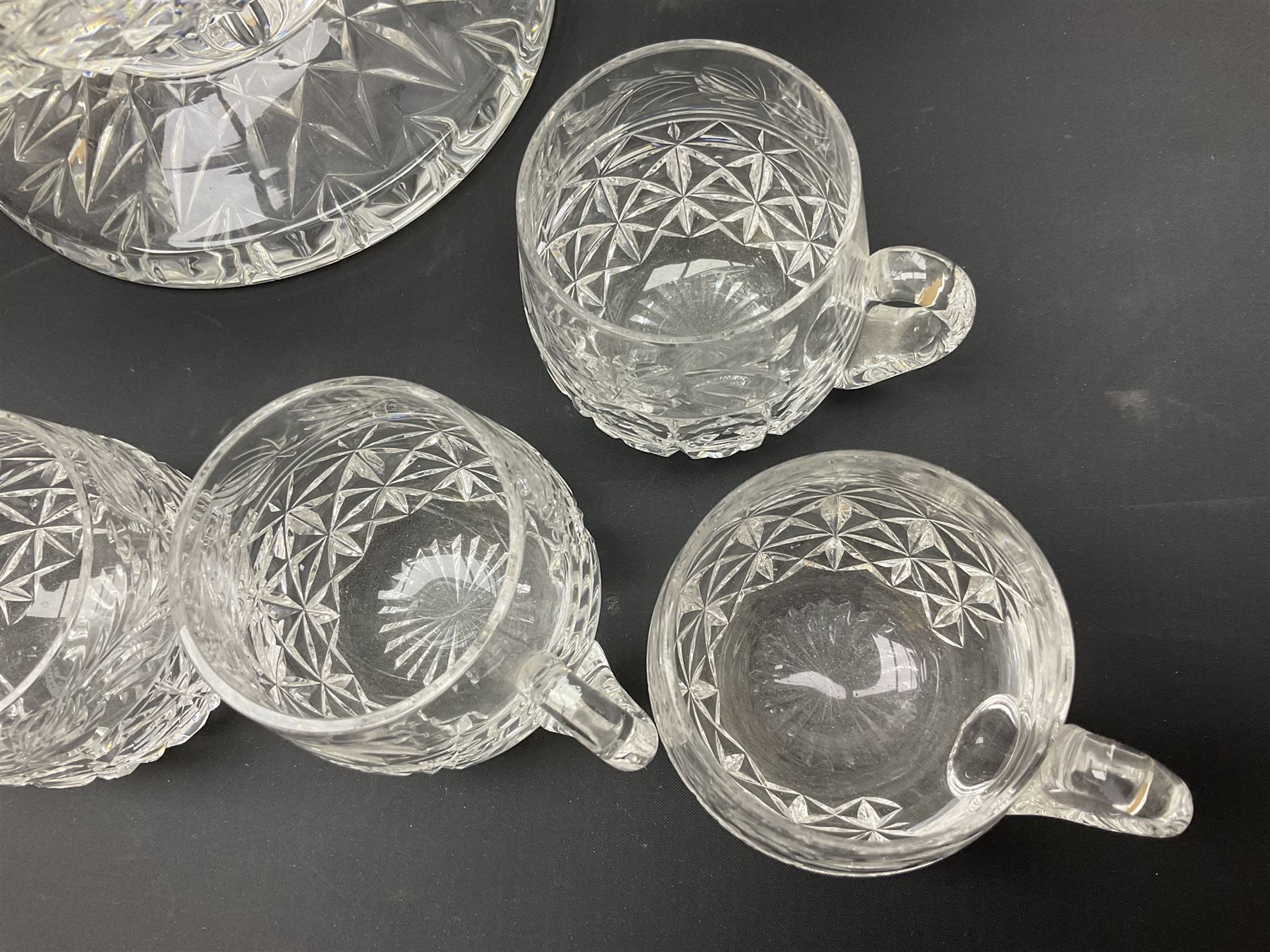 Large Stuart crystal pedestal punch bowl, of circular form, the rim with engraved floral decoration, upon spreading circular foot with radial cut decoration, with seven matching Stuart crystal drinking glasses, each with a C handle, each acid signed beneath, bowl H20cm