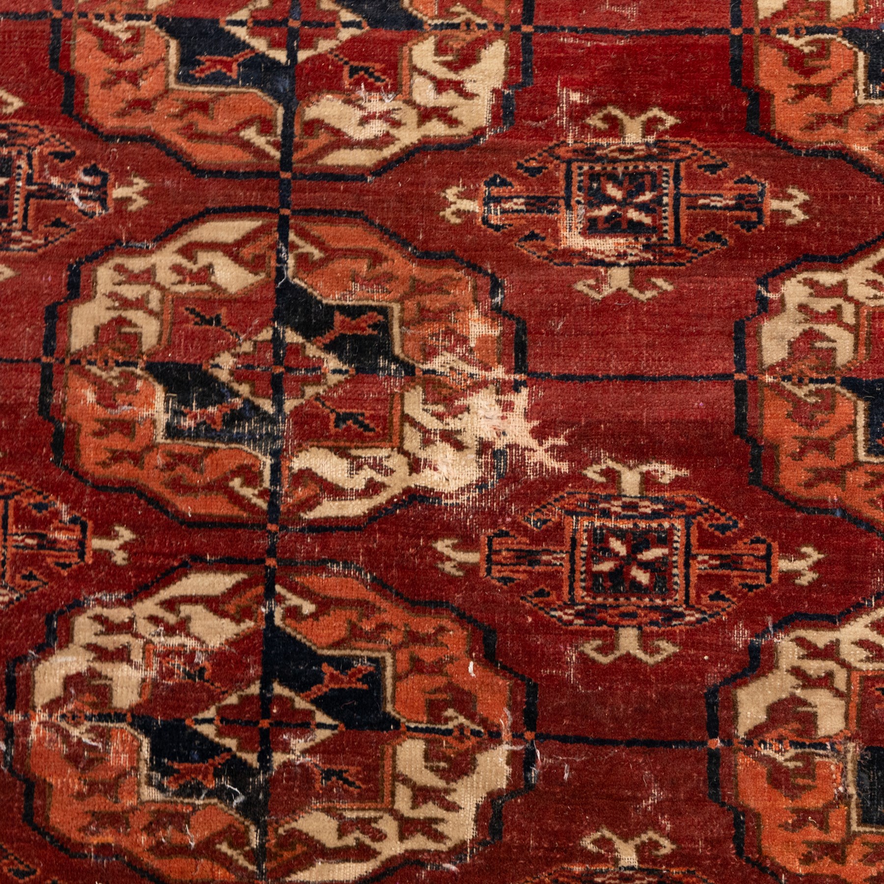 Persian Bokhara crimson ground rug, the field decorated with five rows of repeating Gul motifs with interspersed geometric design, enclosed by a guard band of further geometric-style Gul designs comprised of hook motifs