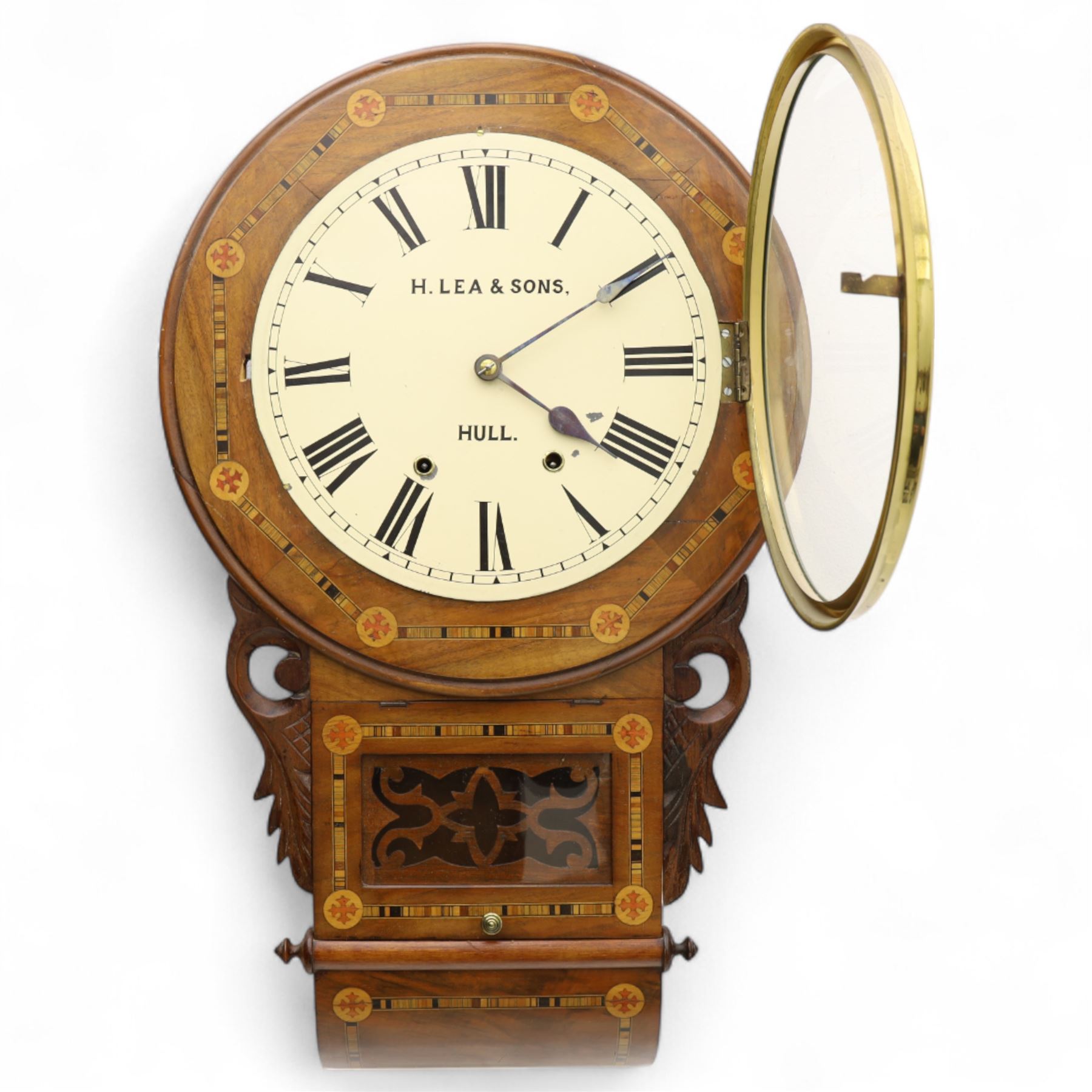 Lea & Son of Hull-American 8-day inlaid mahogany wall clock, with a curved base and carved ears flanking a glazed case door with open fretwork, 12” painted dial with Roman numerals, minute track and spade hands, spring driven movement with a countwheel strike, striking the hours on a bell. With pendulum.
