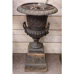  Pair of cast iron two-handled garden urns, lobed and scroll cast bodies on square bases and laurel wreath cast pedestals, H110cm, another similar urn with lion mask handles on plain tapering pedestal, H87cm (3)  