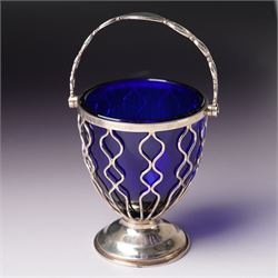 Edwardian pierced silver sugar basket with swing handle and blue glass liner H9cm London 1906 Maker Haseler Bros. and another decorated with floral swags Chester 1912 Maker  (2)