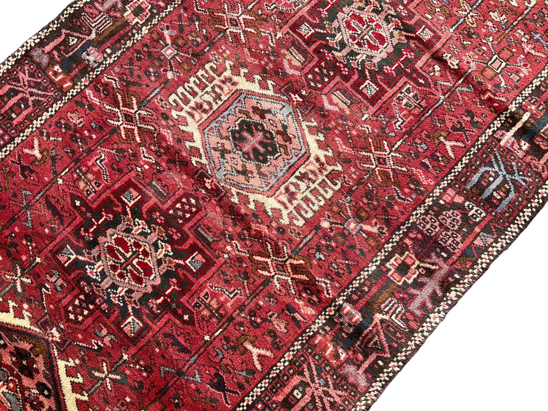 Persian Karajeh crimson ground runner rug, the field set with seven geometric lozenge medallions, the field decorated all over with stylised plant motifs, the banded border with repeating geometric shapes and patterns