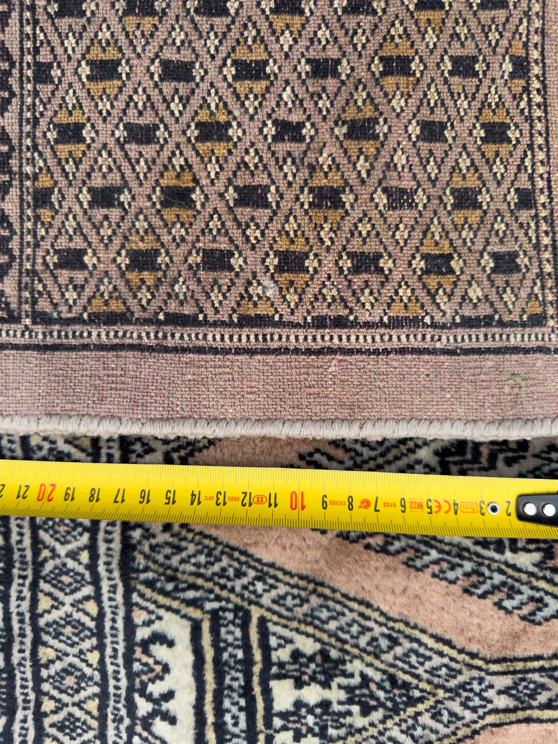 Large Persian Bokhara wool rug, the field decorated with repeating gul motifs in lozenge medallions across a dark ground, enclosed by multiple geometric borders in indigo, ivory and terracotta, from the region of Baluchistan