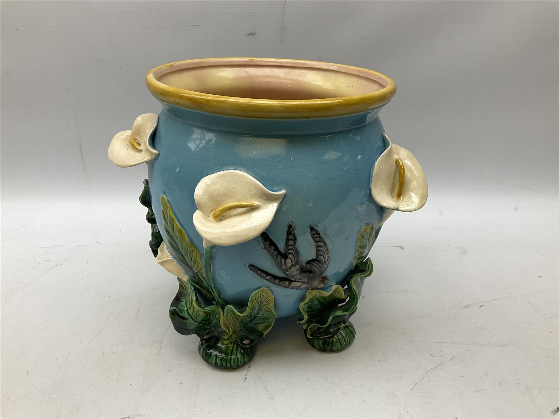 George Jones style majolica jardiniere of globular form, supported on four feet formed from modelled lily leaves growing up the side of the pot, with swallows flying amongst the white lily flowers, all set against a blue ground, with a pink interior, H27cm
