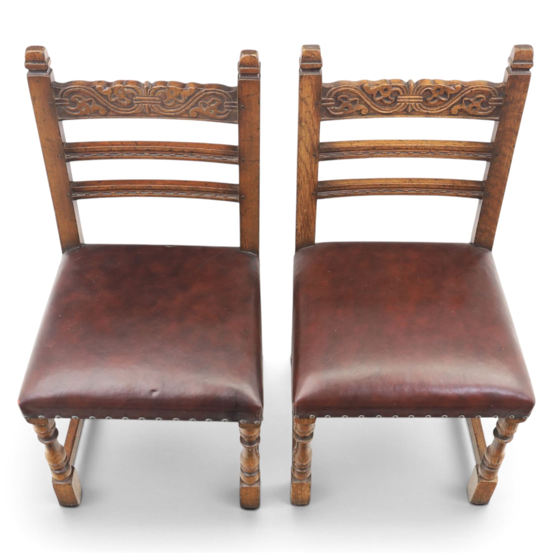 Craftsman made set of four solid oak dining chairs with leather seats, with carved cresting rail, on red leather seats with studded trim, raised on block and turn supports united by H-stretcher
