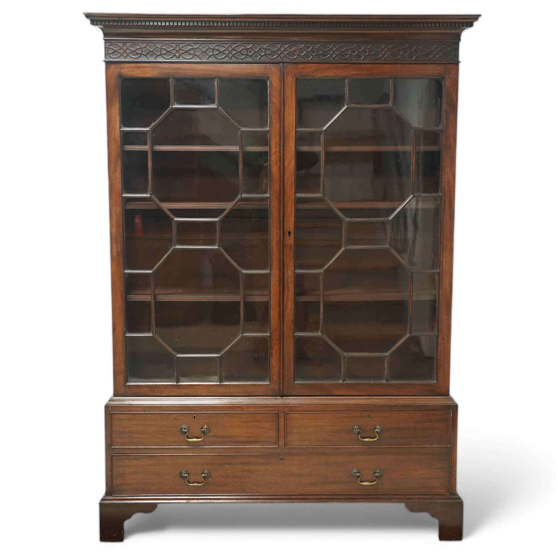 Early 20th century mahogany glazed bookcase, the moulded cornice above a carved frieze with interlaced ornament, enclosed by a pair of astragal glazed doors with geometric glazing bars, the base fitted with two short over two long drawers with brass swan neck handles, raised on bracket feet