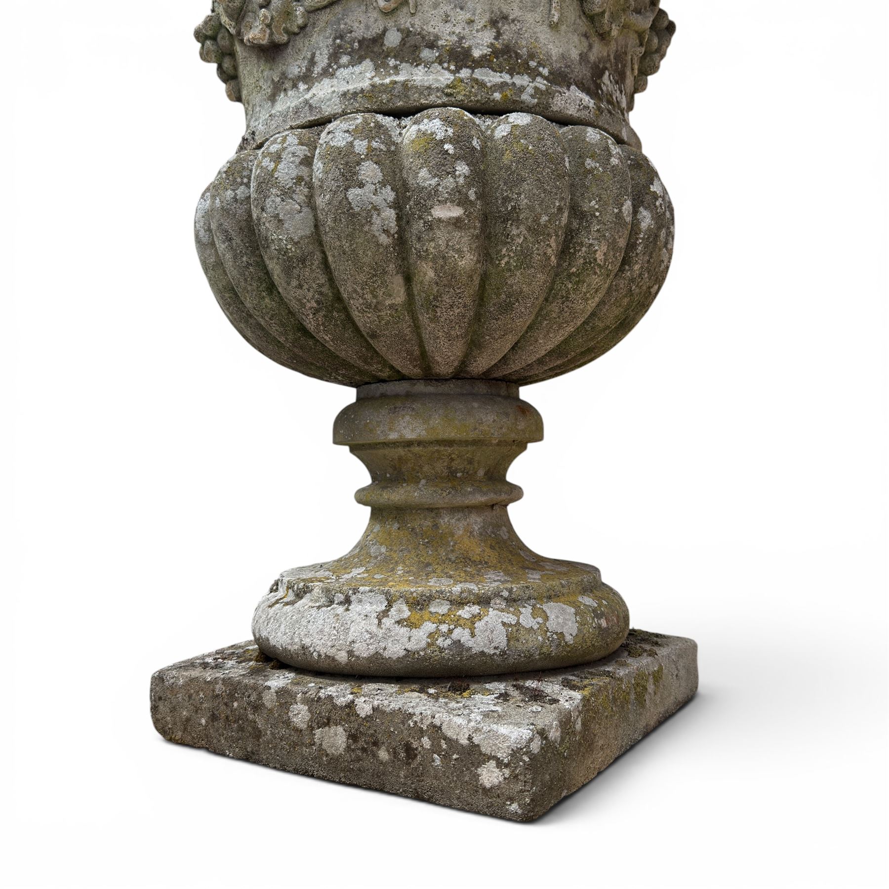 Pair of quality antique weathered three-piece composite stone garden urns, the flared rim moulded with repeating acanthus leaves, over a deep-relief campana body decorated with fruiting grapevines and ivy leaves, the gadrooned underbelly over a turned socle and square base