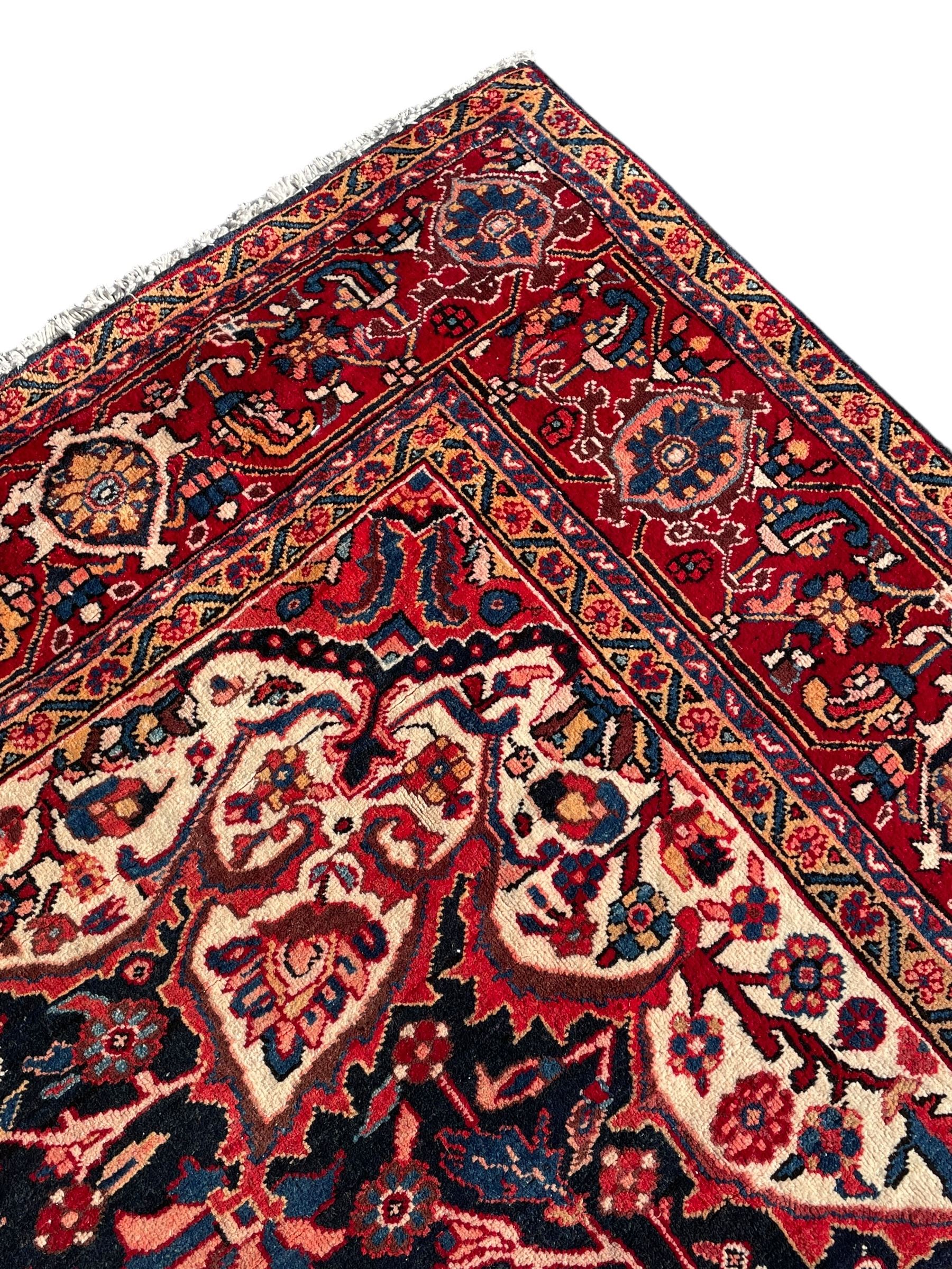 Persian Hamadan indigo and red ground carpet, large central medallion decorated with projecting palmette motifs, the surrounding field decorated with trailing branches and flower heads, crimson ground border decorated with stylised plant motifs, within floral pattern guard stripes 