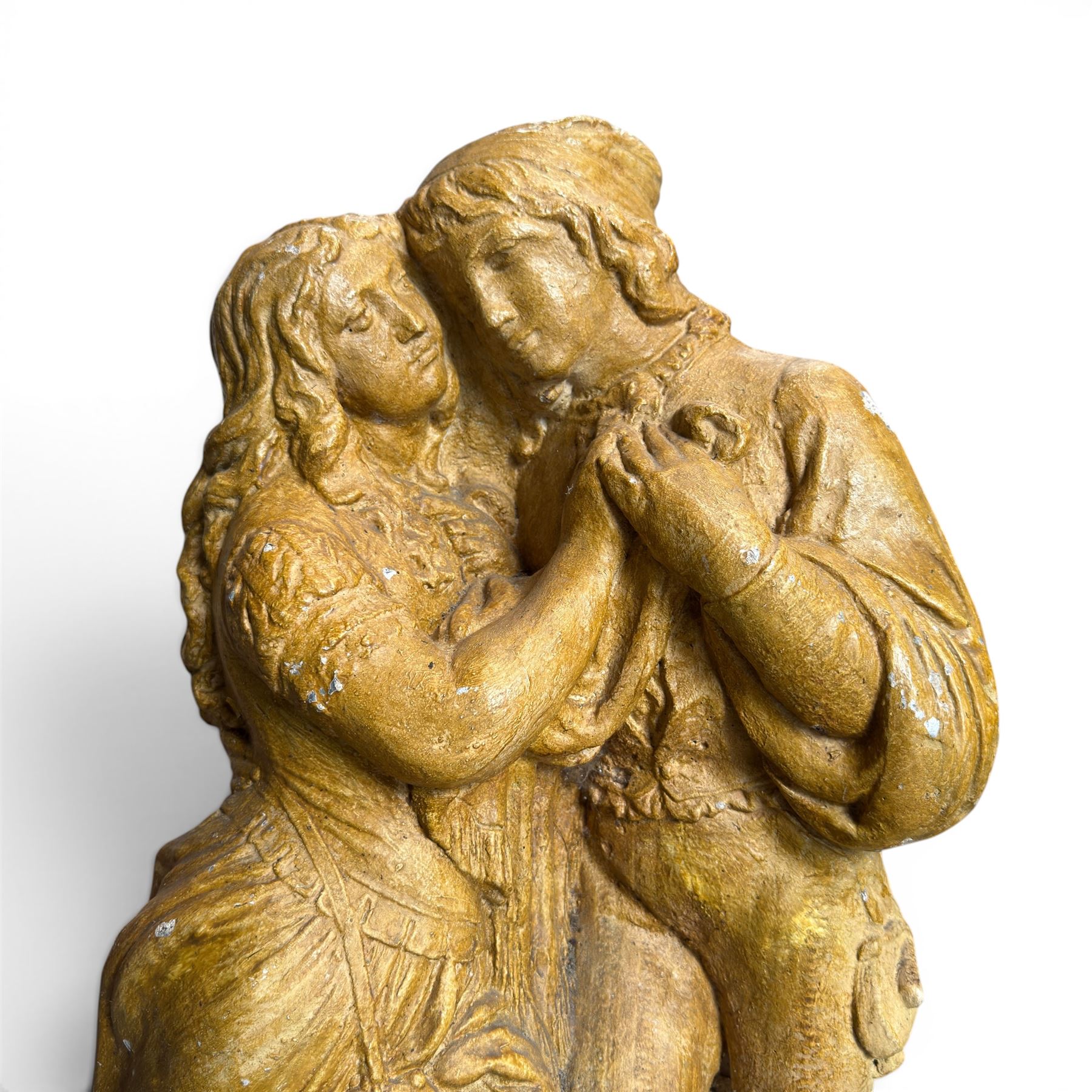 Composite garden statue group of Romeo and Juliet embracing in Medieval dress, surmounted on a naturalistic foliate base, in antique distressed glazed finish